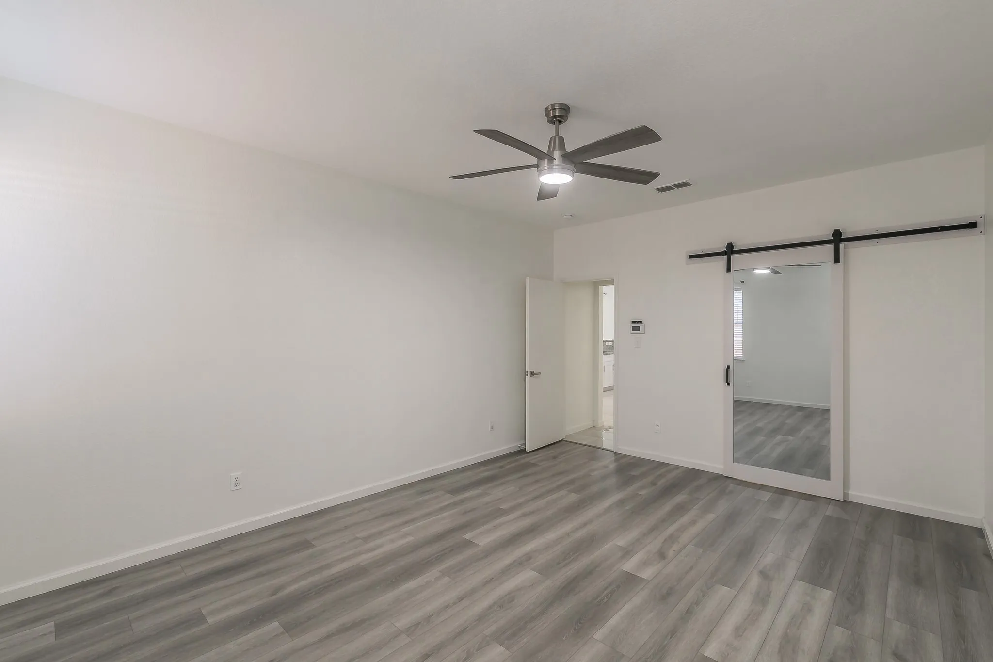 Unfurnished bedroom with a ceiling fan, visible vents, a barn door, wood finished floors, and baseboards