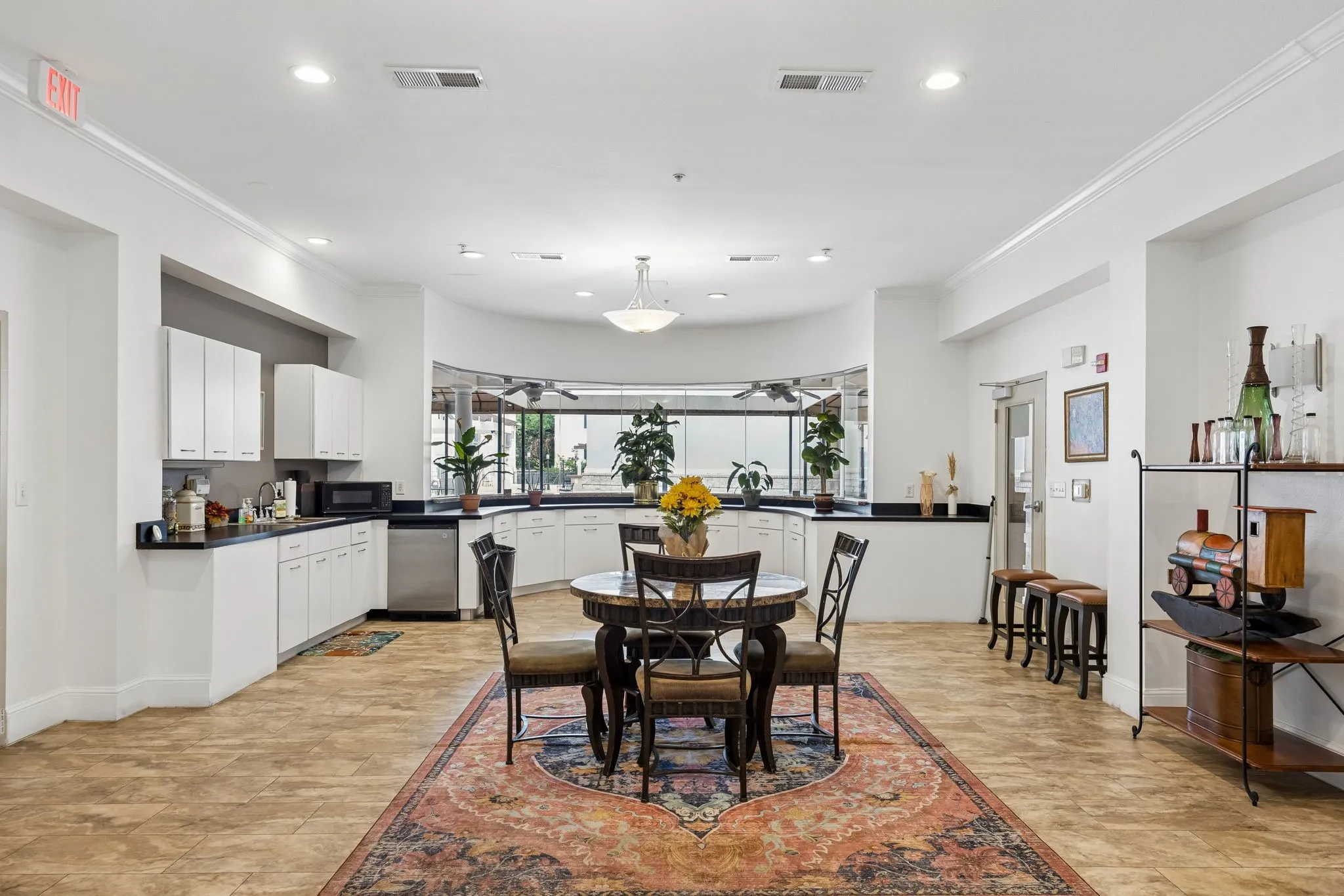 Spacious common area featuring light-toned tile flooring, recessed lighting, and a kitchen area with white cabinetry and dark countertops