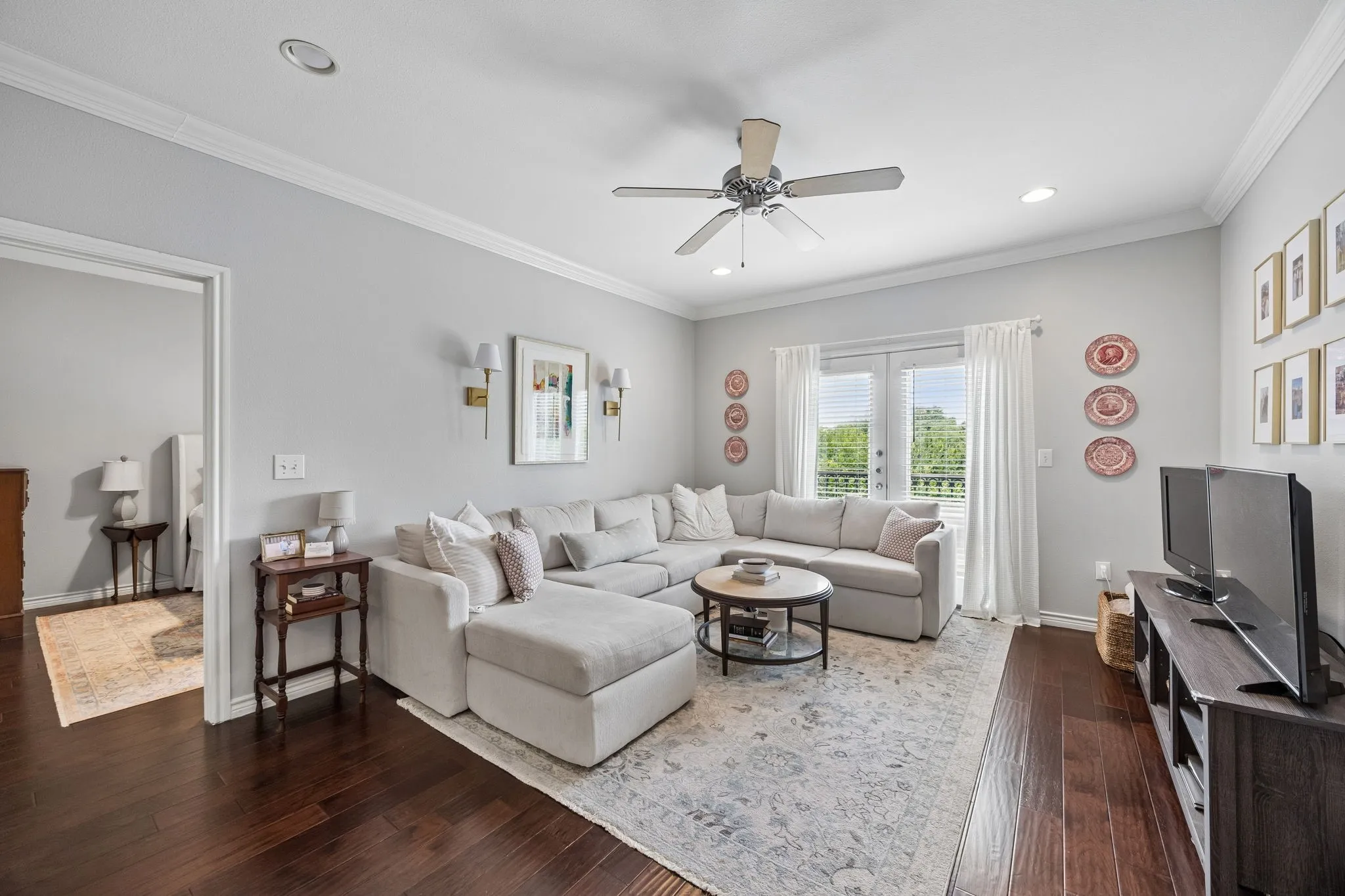 Spacious living area featuring rich wood-finish flooring, crown molding, recessed lighting, and a ceiling fan
