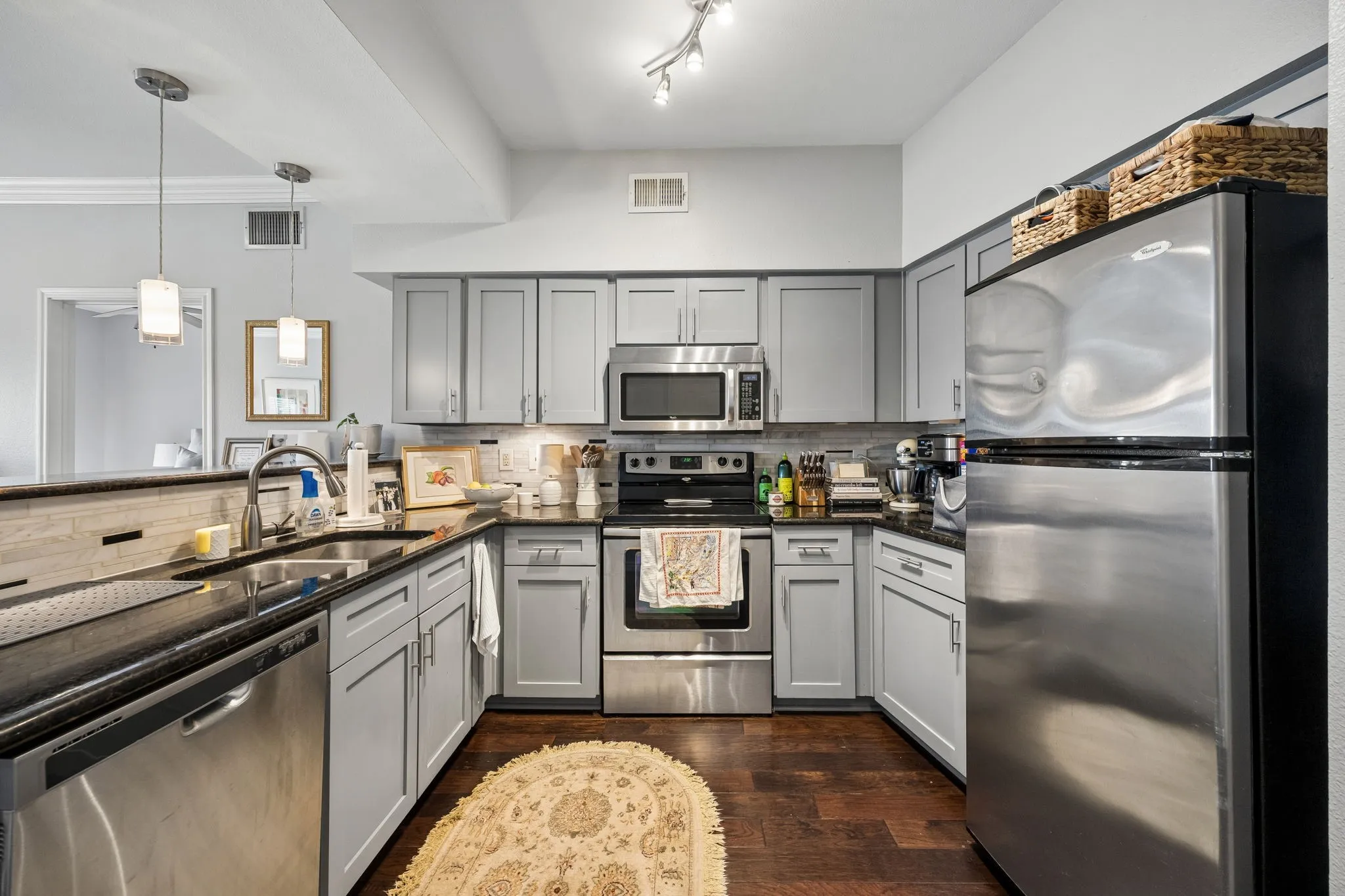 Well-appointed kitchen featuring light gray cabinetry, stainless steel appliances, dark countertops, a tiled backsplash, and recessed and pendant lighting