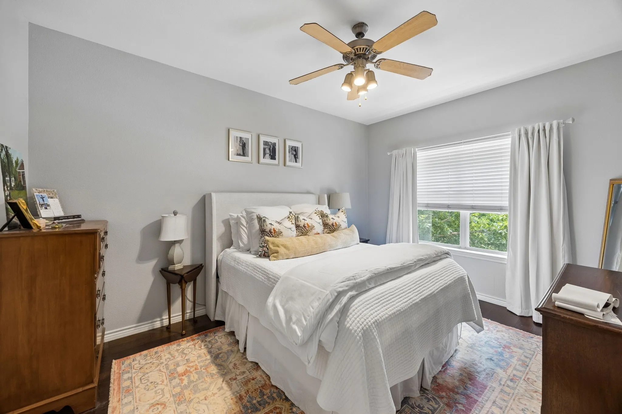 Interior room featuring wood-finish flooring, a ceiling fan with light fixture, and a window with blinds and curtains