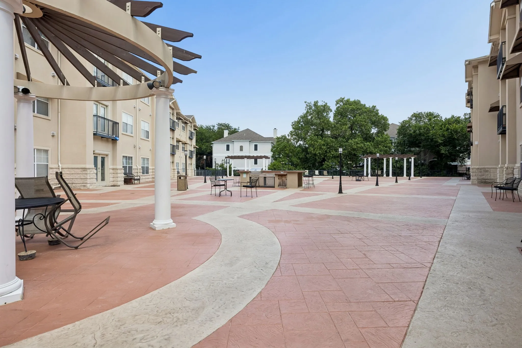 Expansive paved courtyard featuring decorative pergolas, outdoor lighting, and a built-in outdoor kitchen area