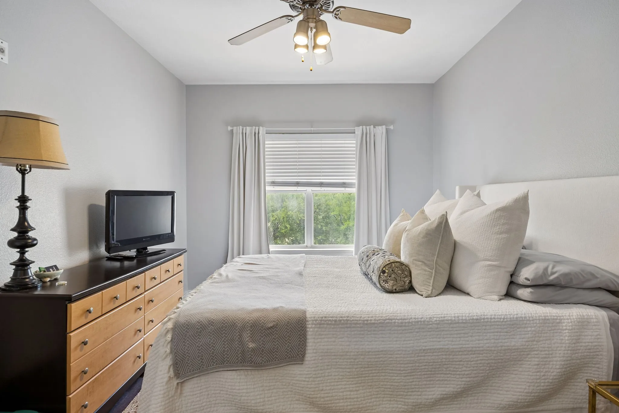 Bright room with a ceiling fan, window with blinds and drapes, and light gray walls