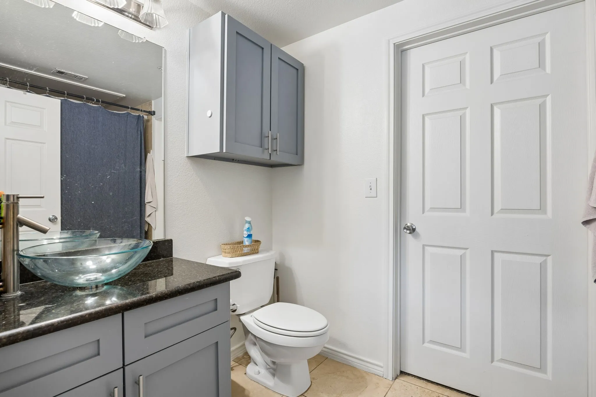 Bathroom featuring a vessel sink, dark stone-finish countertop, light gray cabinetry, and neutral tile flooring