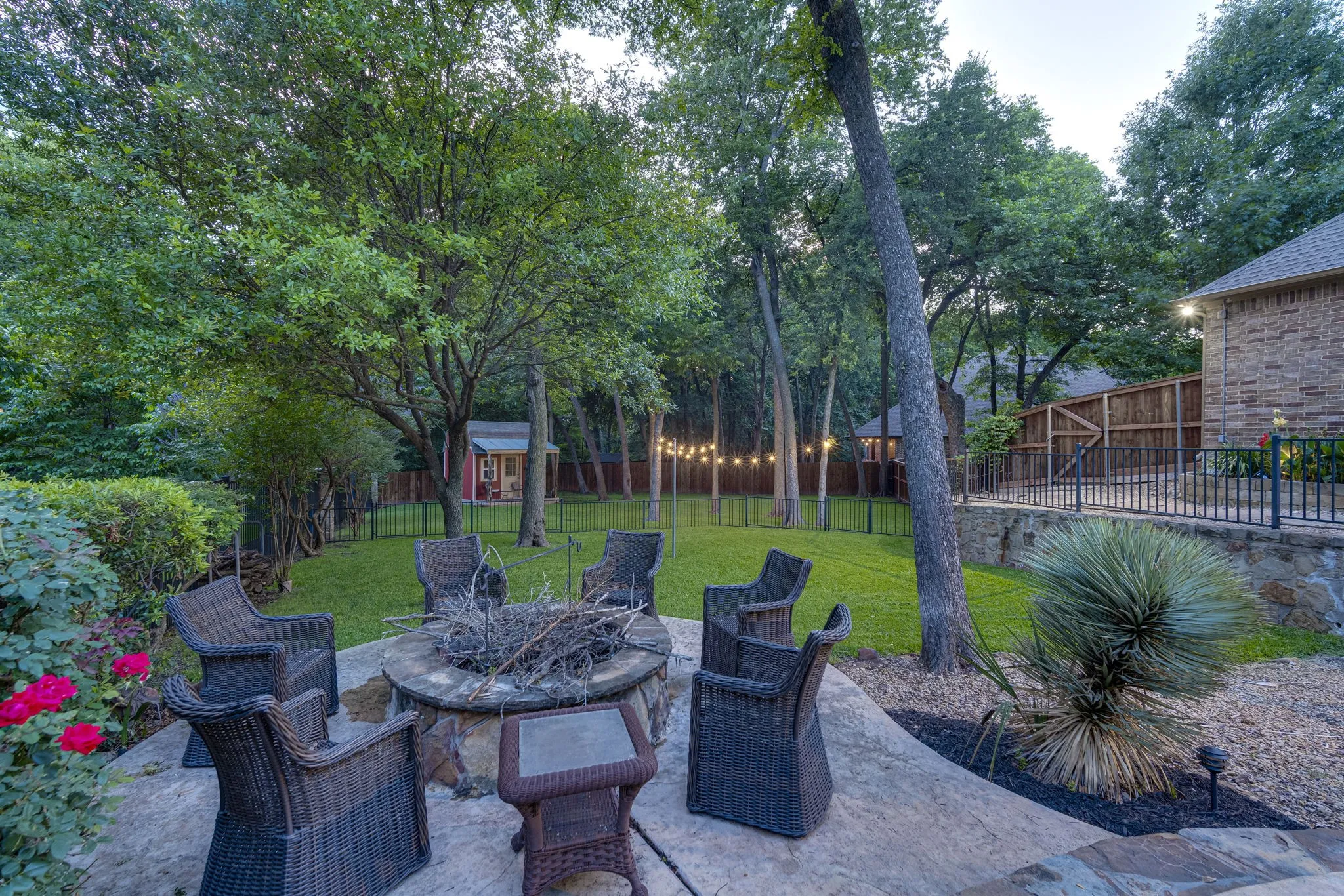 Cozy fire pit gathering area tucked beneath a canopy of mature shade trees.
