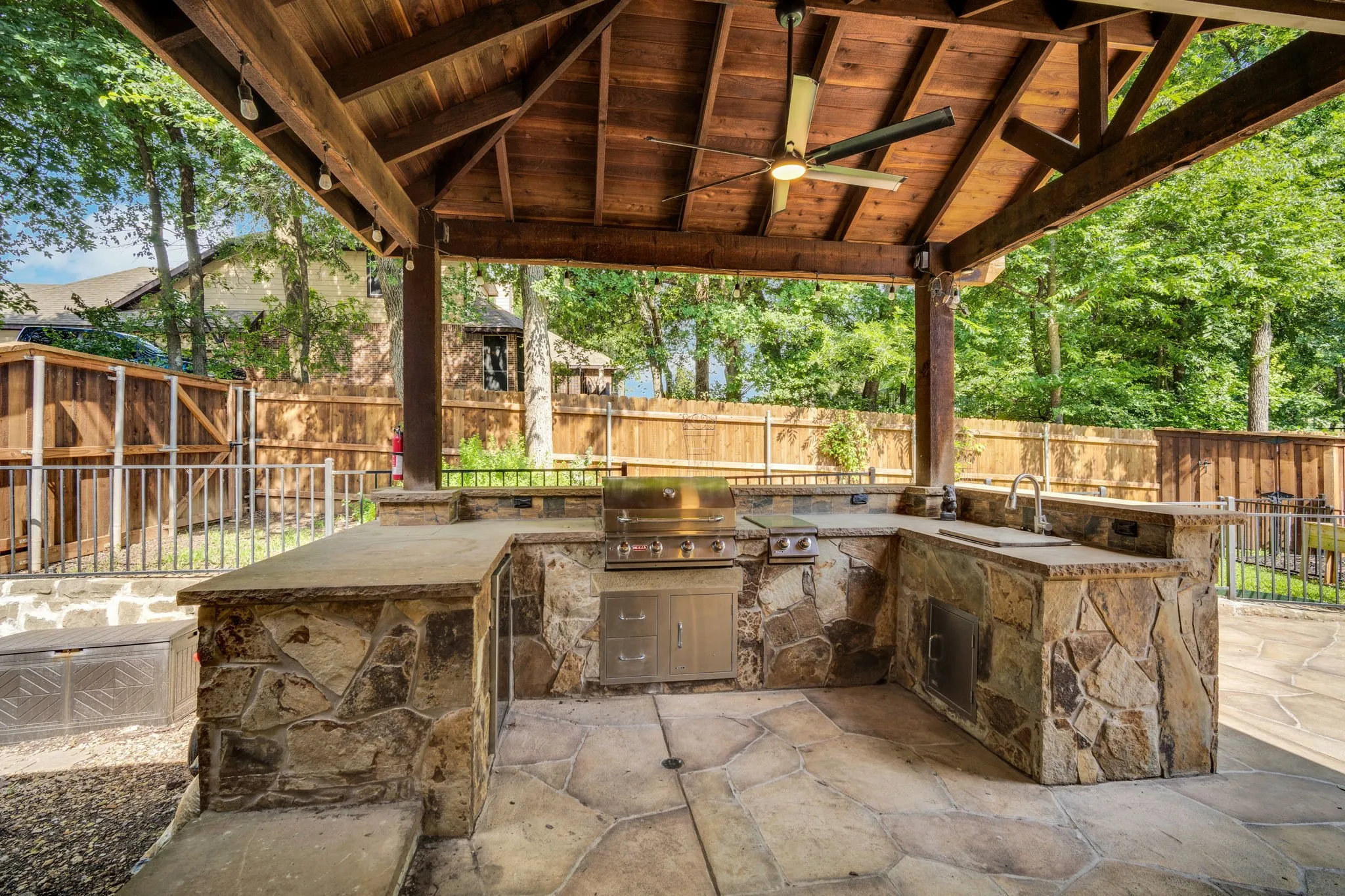 Covered outdoor kitchen pavilion with a stone bar, perfect for entertaining beneath the trees.