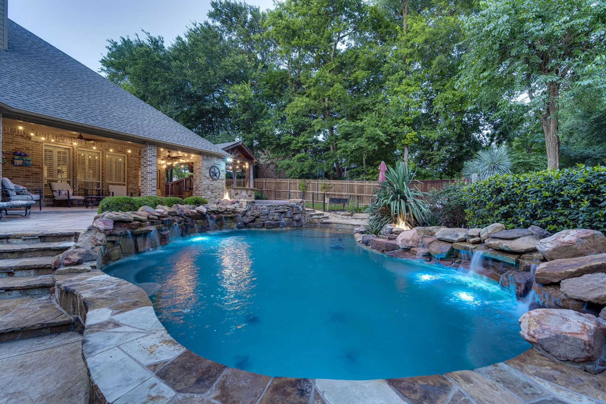 Sparkling pool with a cascading rock waterfall, framed by a covered outdoor living pavilion.