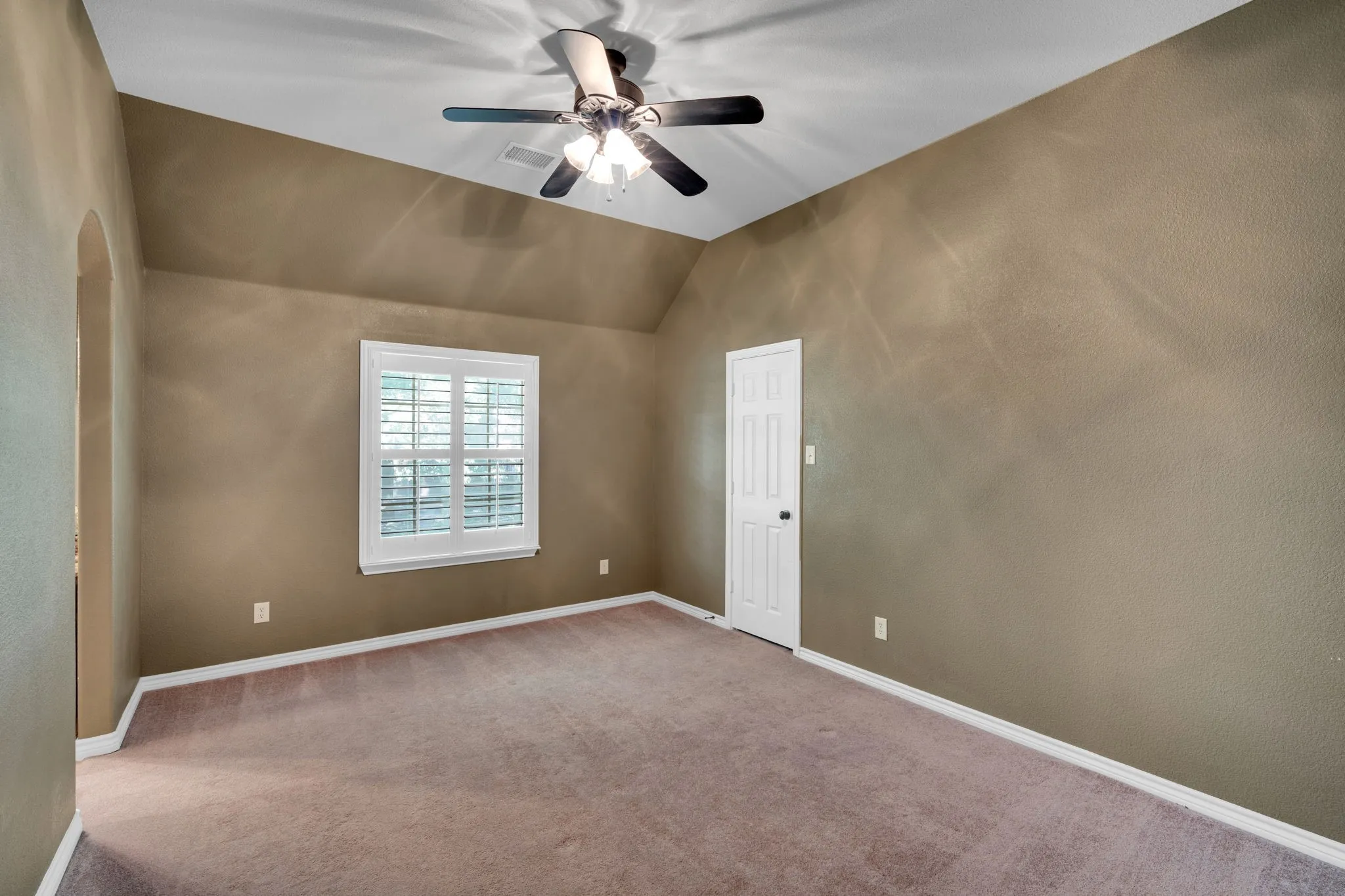 Bedroom with a vaulted ceiling and a large window.
