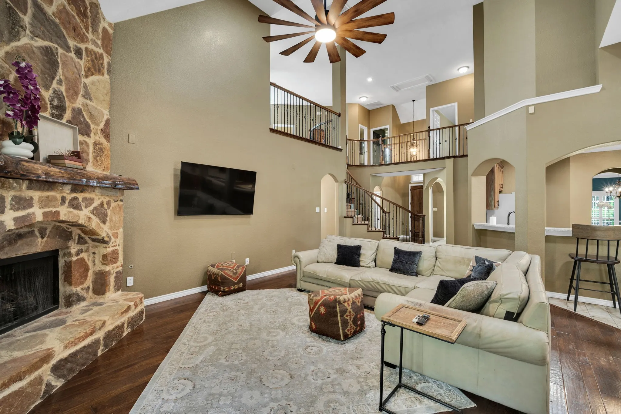 Dramatic two-story living room anchored by a stone fireplace and an open staircase overlook.