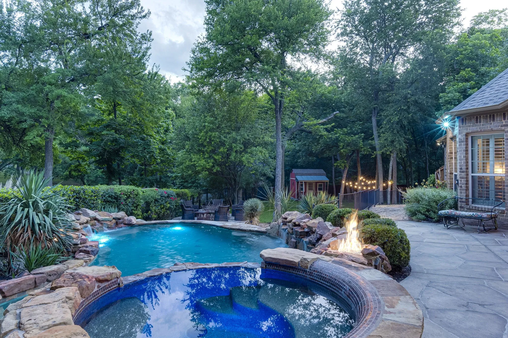 Backyard oasis featuring a resort-style pool with a natural rock waterfall, surrounded by lush mature trees.