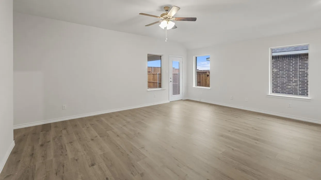 Spacious interior room featuring wood-finish flooring, white walls, and a ceiling fan with integrated lighting
