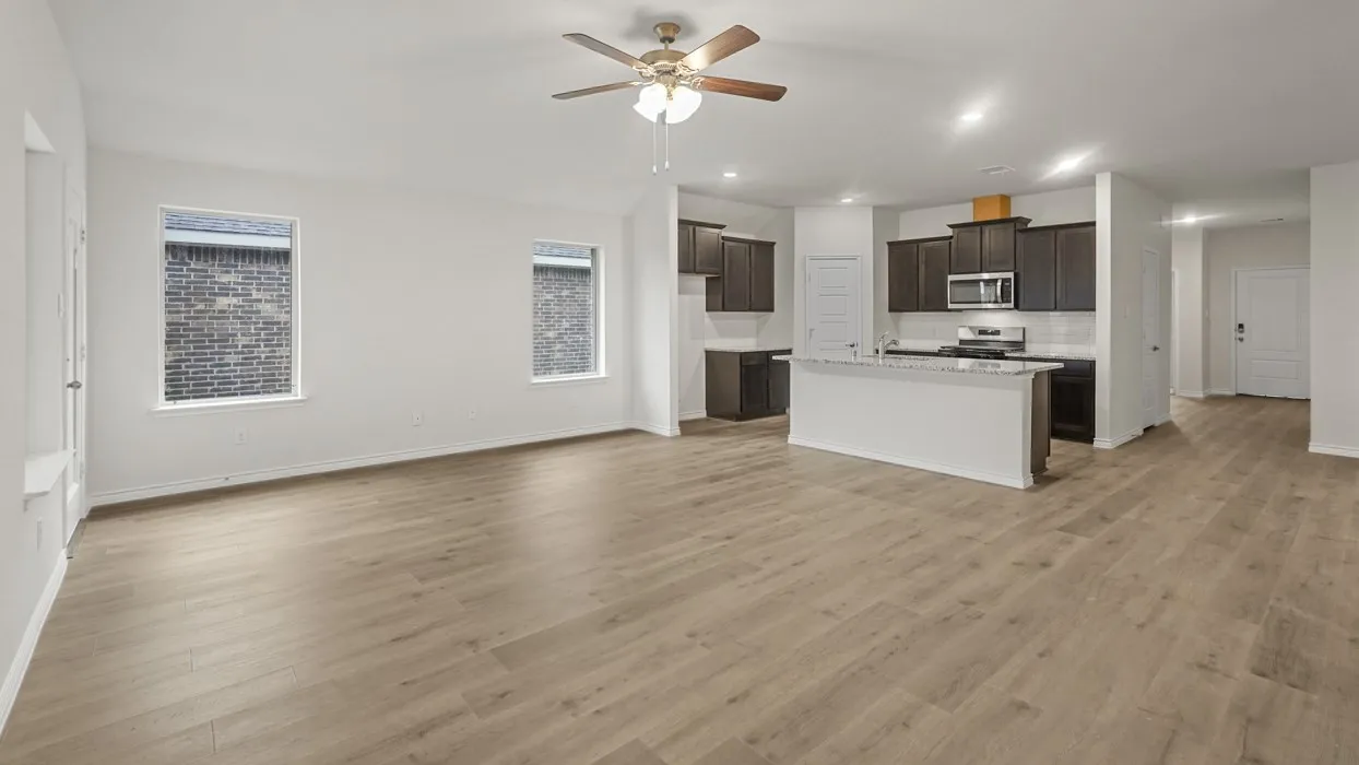 Spacious living area featuring wood-finish flooring, two windows, and a ceiling fan with integrated lighting