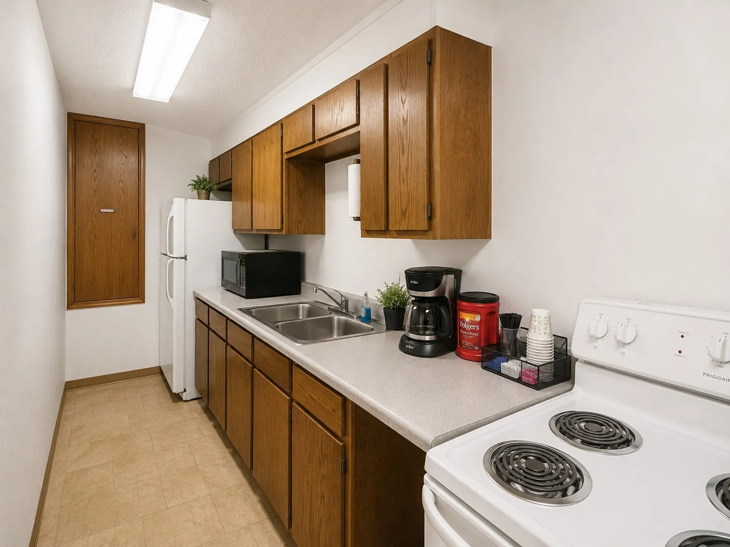 Kitchen featuring wood cabinetry, laminate countertops, a double basin stainless steel sink, and a white electric range