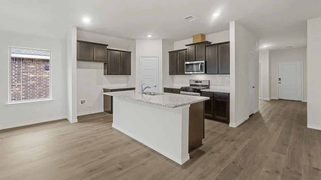 Open-concept kitchen featuring an island with a built-in sink, wood-finish flooring, dark wood cabinetry, stainless steel appliances, and white subway tile backsplash