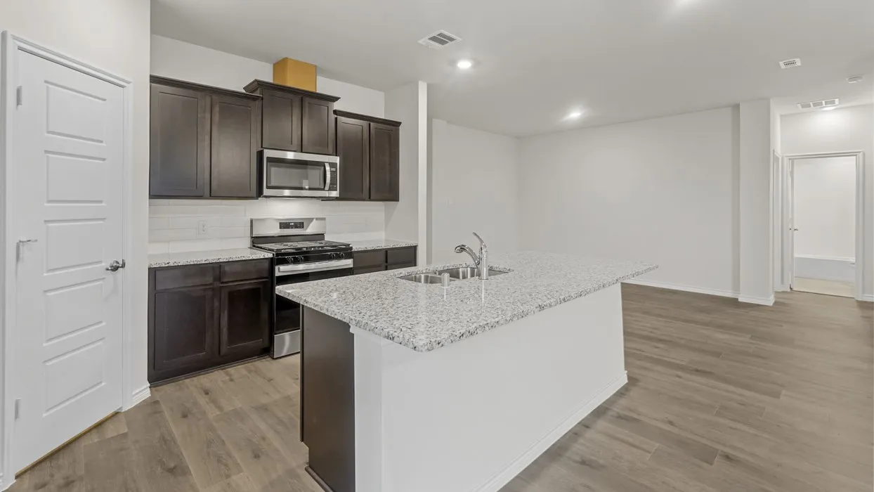 Modern kitchen featuring dark wood cabinetry, stainless steel appliances, a subway tile backsplash, and light-toned granite countertops
