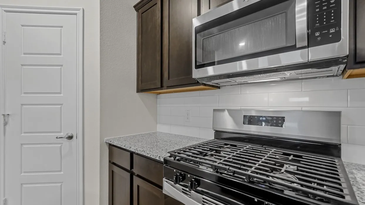 Modern kitchen featuring dark wood cabinetry, granite-finish countertops, stainless steel appliances, a gas range, and a white subway tile backsplash