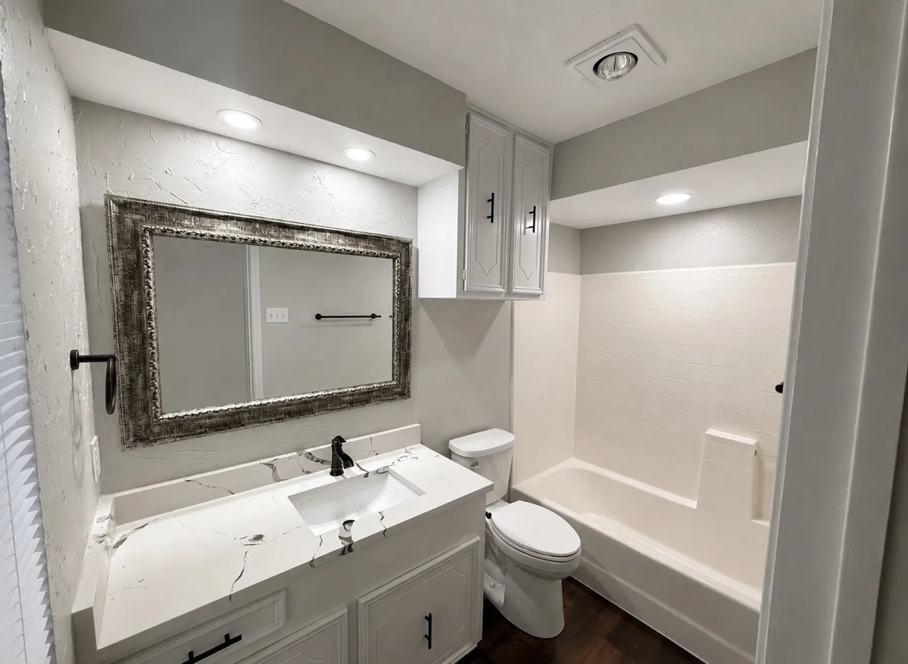 Modern bathroom featuring a vanity with a rectangular sink, a light-toned countertop with dark veining, and dark wood-finish flooring