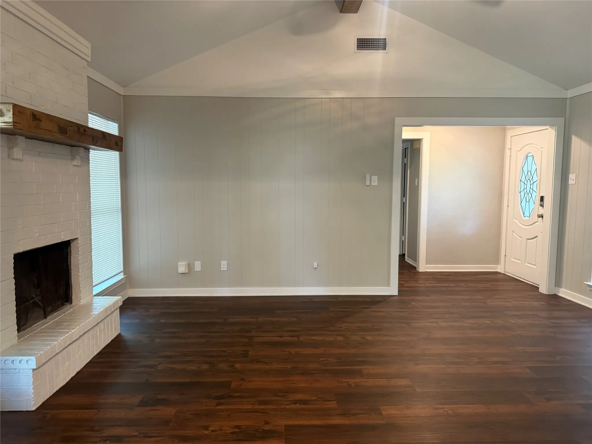 Spacious living area featuring high vaulted ceilings, wood-finish flooring, and a whitewashed brick fireplace with a substantial timber mantel
