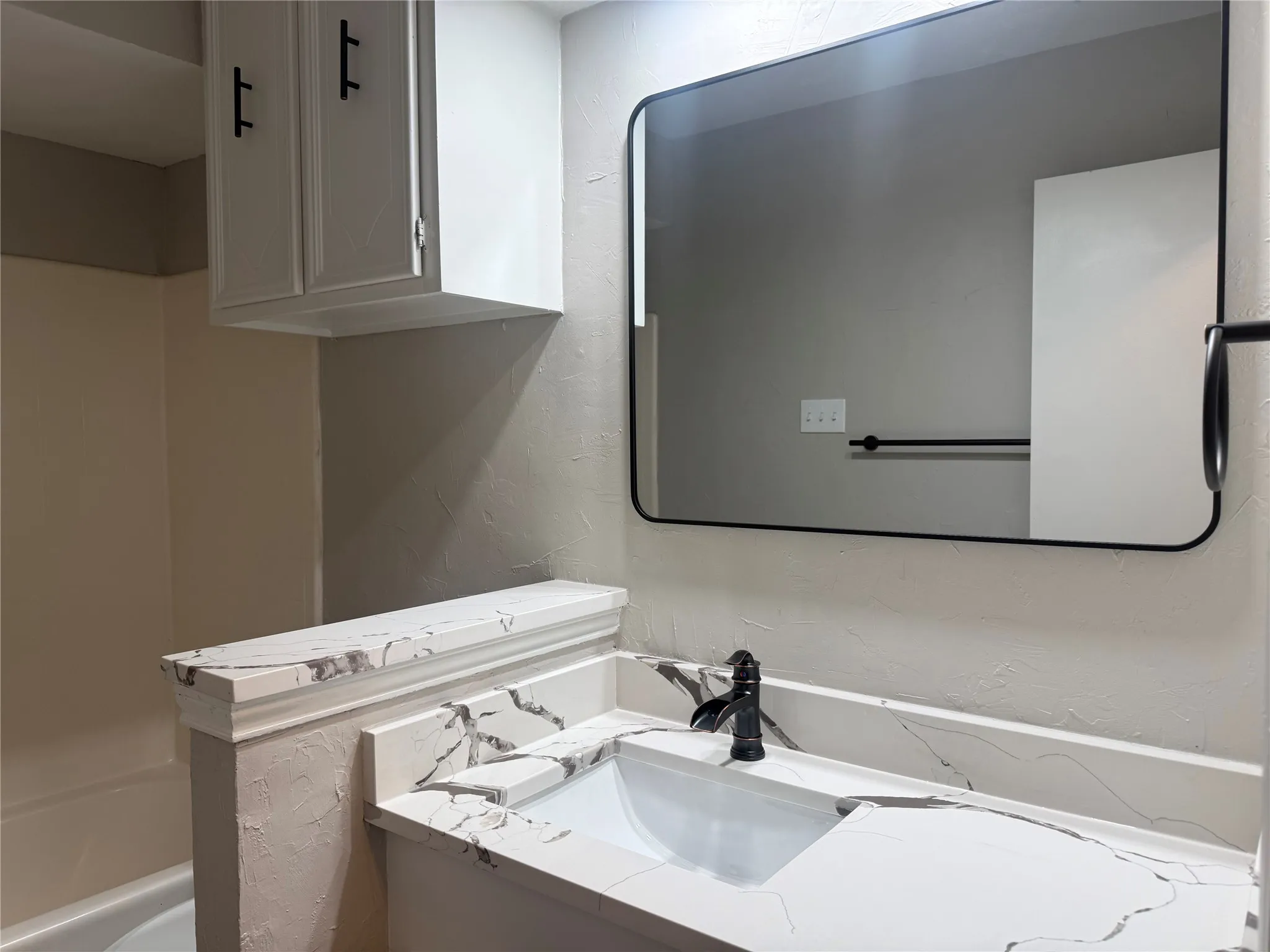 Bathroom vanity featuring a single integrated sink with a black faucet, white countertop with dark veining, and a contemporary black-framed rectangular mirror