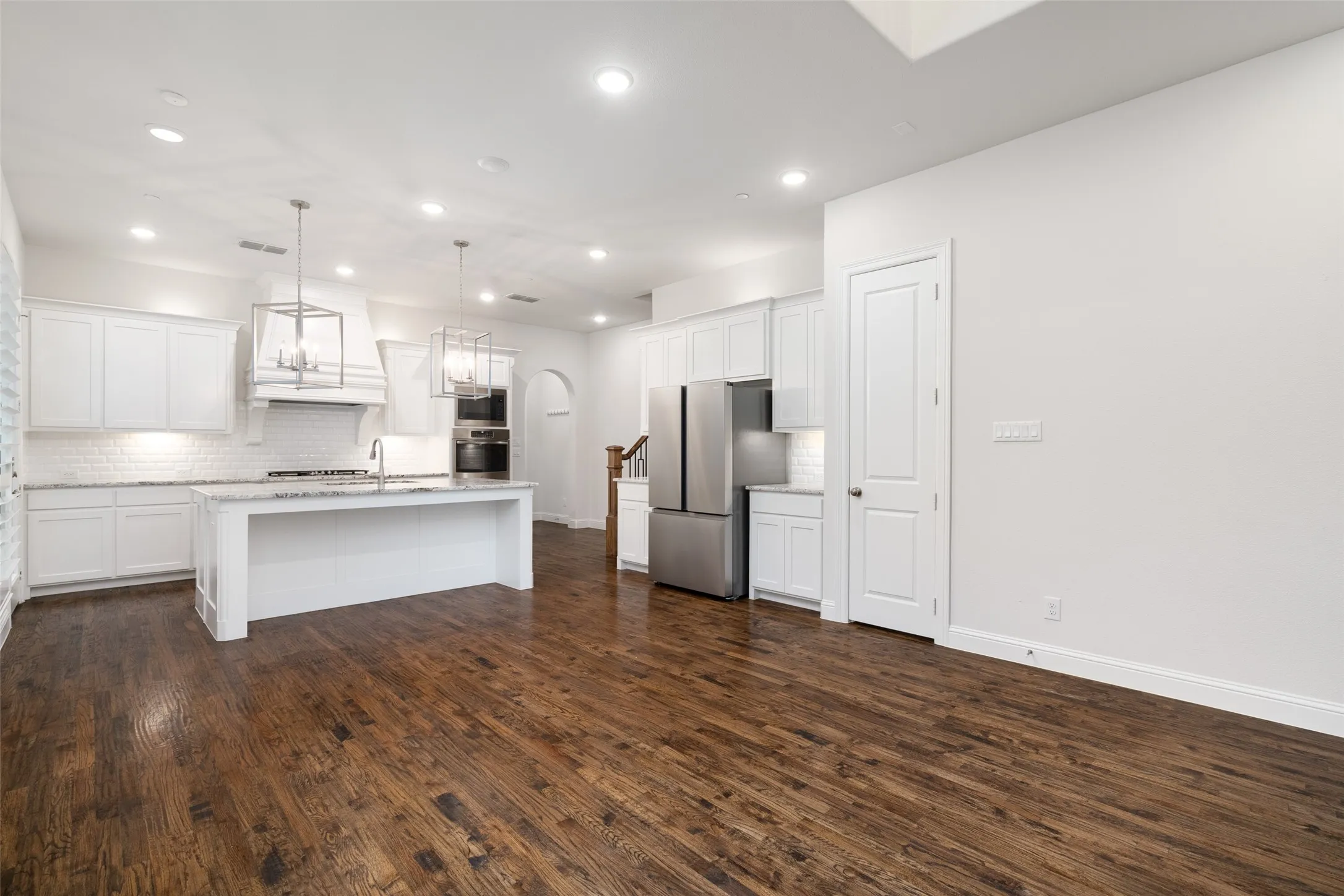 The bright, open-concept dining & kitchen; crisp white cabinetry, rich hardwood floors and a spacious center island: Features include stainless-steel appliances, refrigerator, a gas cooktop, subway-tile backsplash, statement pendant lighting and a custom vent hood.