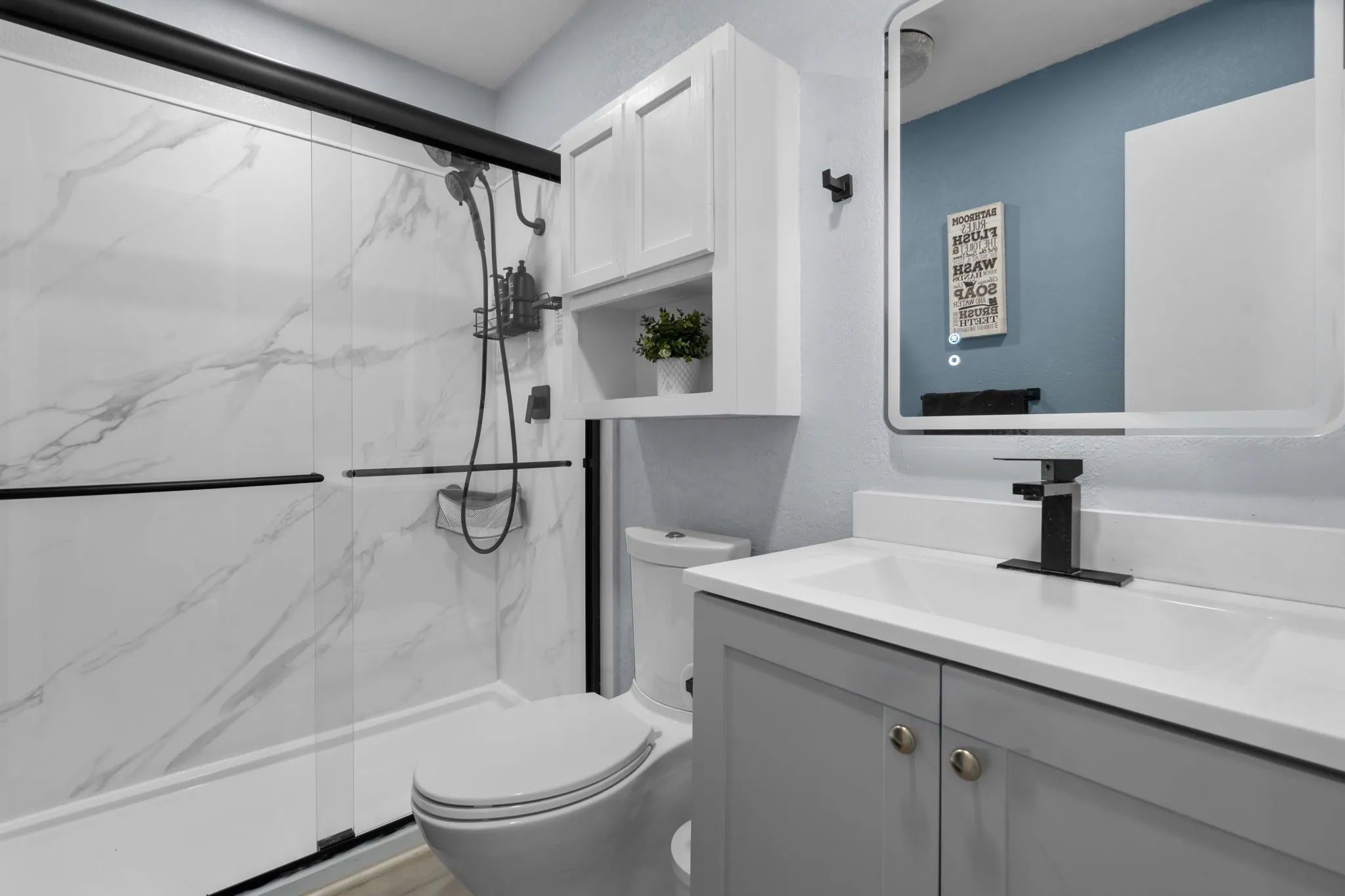 Modern bathroom featuring a walk-in shower with marble-look paneling and black-framed sliding glass doors