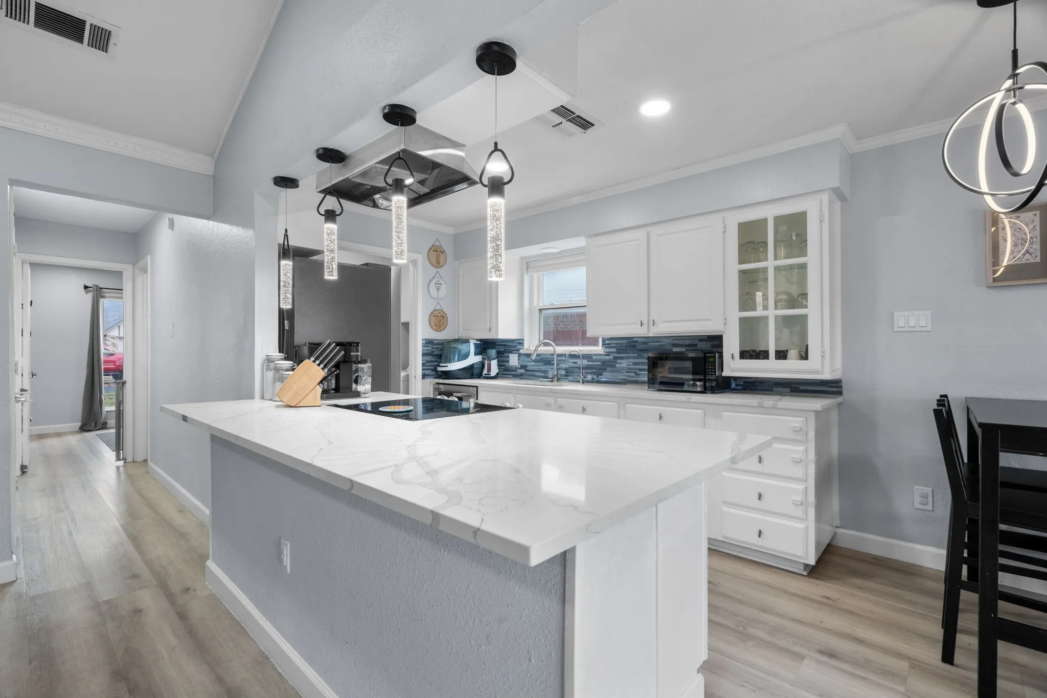 Modern kitchen featuring a large central island with a cooktop, white cabinetry, a blue tile backsplash, recessed lighting, and wood-finish flooring