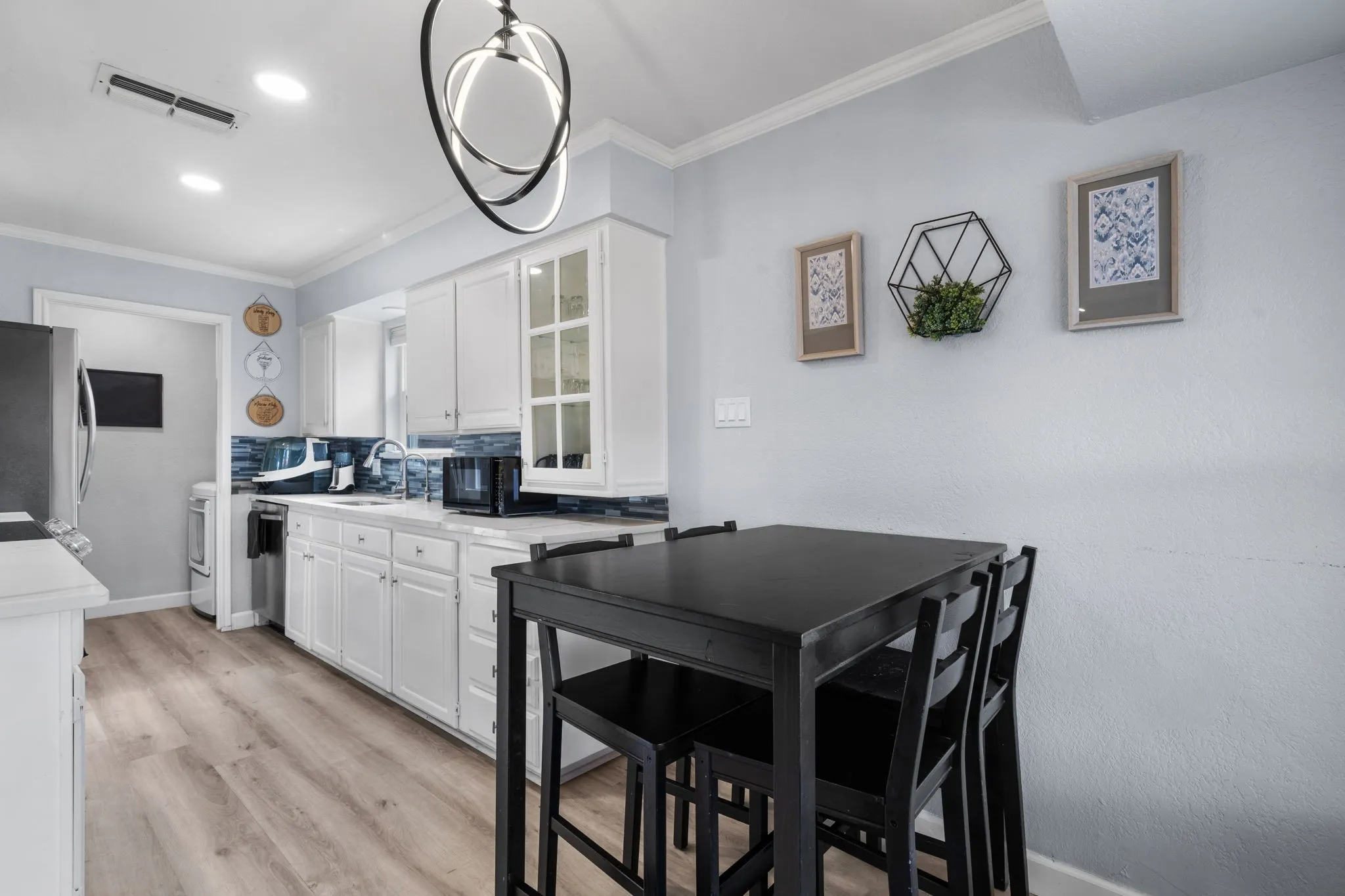 Kitchen featuring white cabinetry with glass-front accents, light-tone wood-finish flooring, and a blue tile backsplash