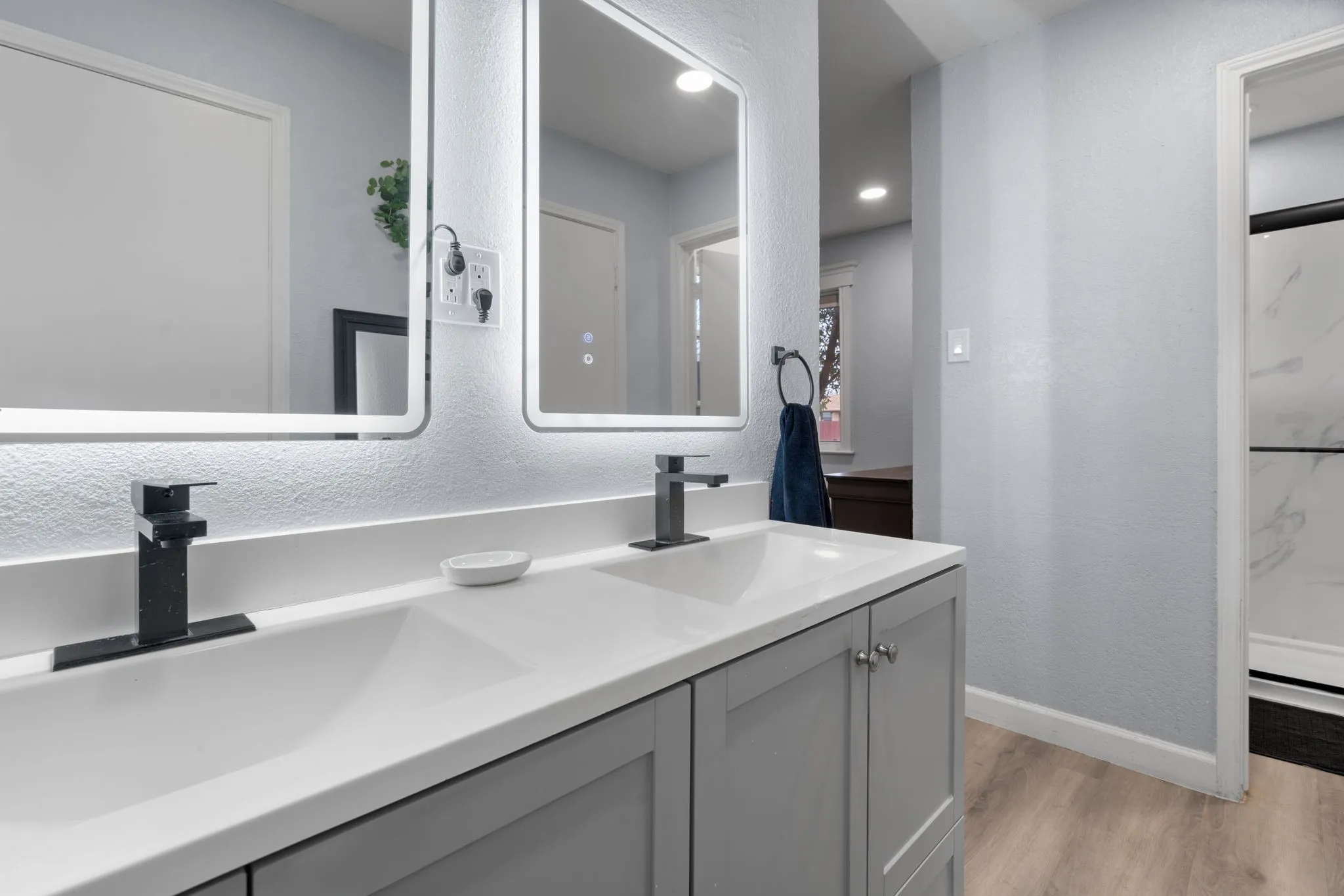 Dual vanity with integrated sinks, white countertops, gray shaker cabinetry, matte black faucets, and illuminated rectangular mirrors