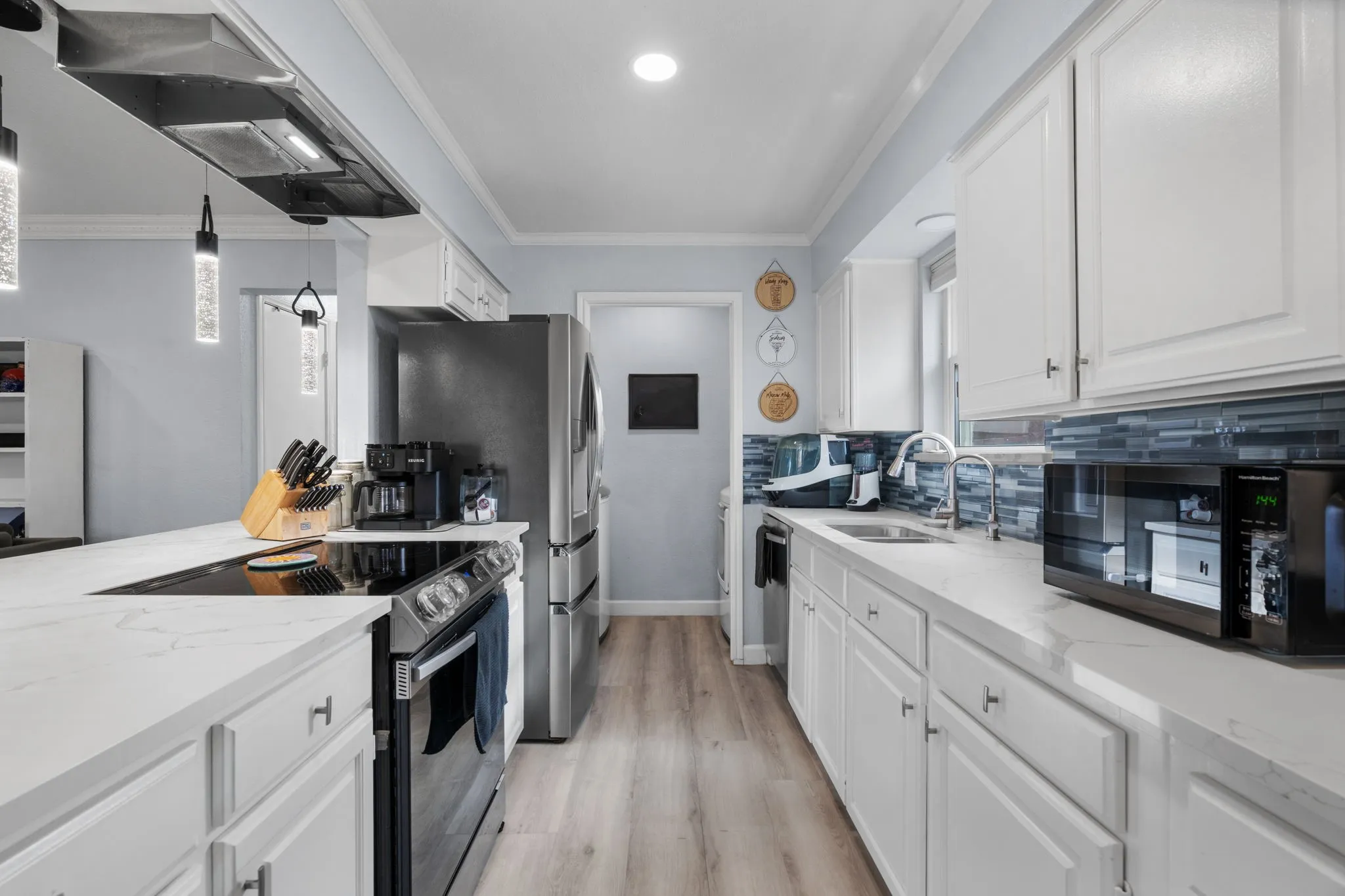 Modern kitchen featuring white cabinetry, light-toned countertops, and a full suite of stainless steel appliances including a refrigerator and range