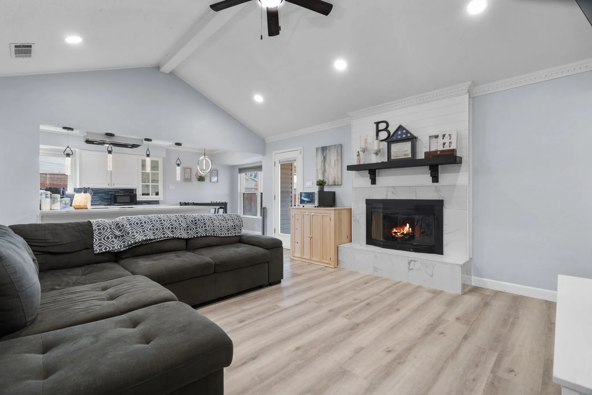 Vaulted ceiling living area featuring a fireplace with a white shiplap and marbled-look surround, recessed lighting, wood-finish flooring, and a ceiling fan