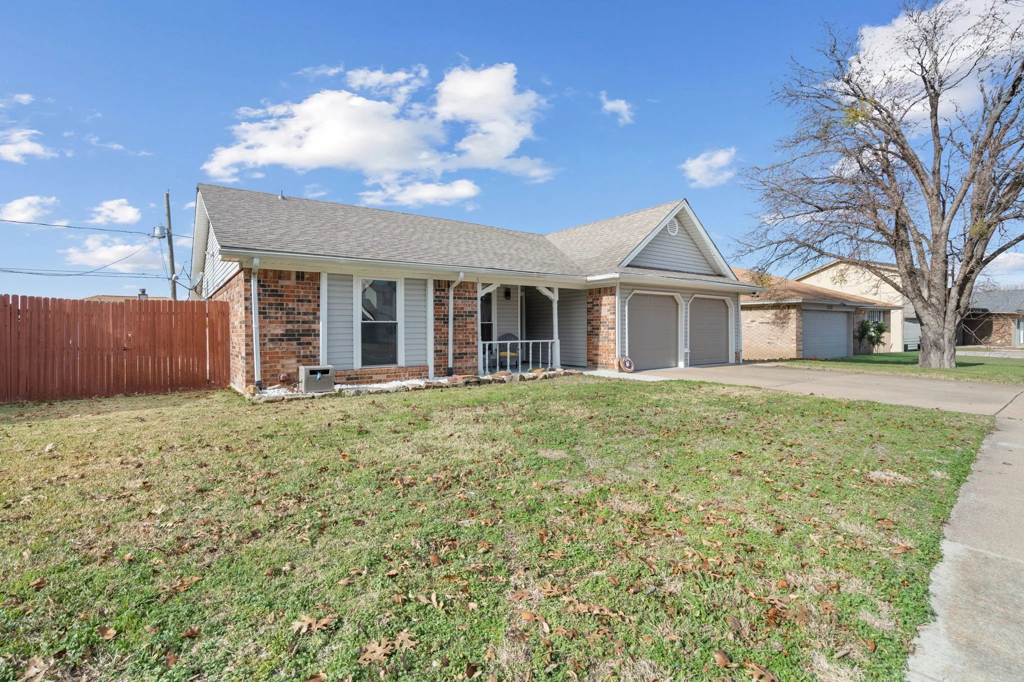 Brick and siding exterior featuring a covered porch with white railing, a two-car garage with individual doors, and a partial wooden privacy fence
