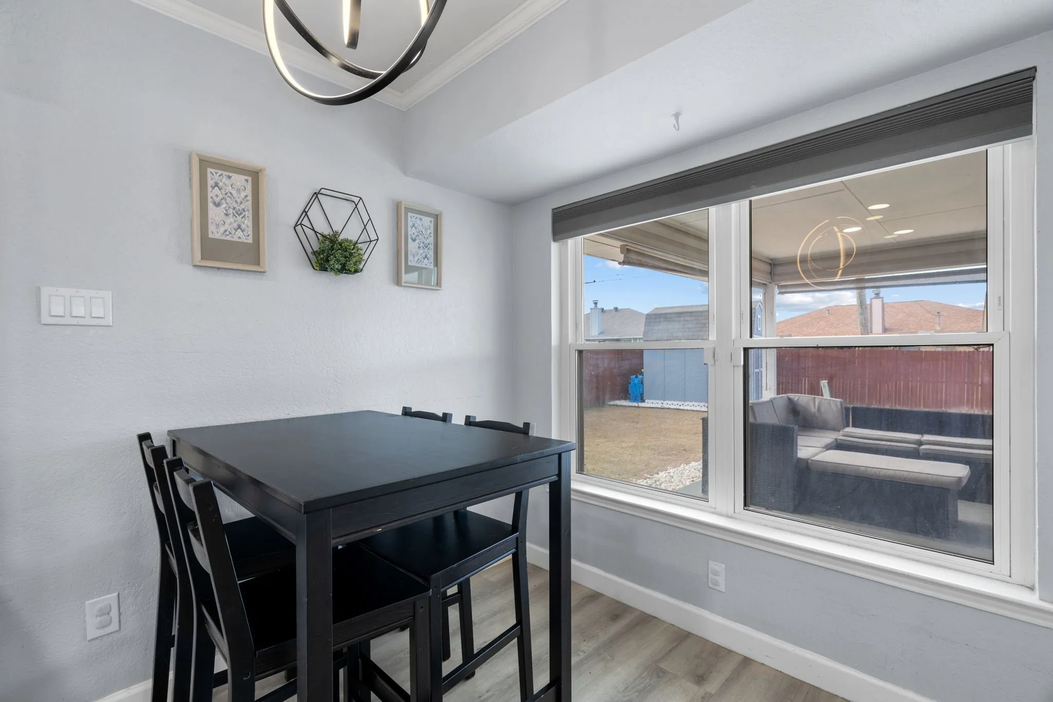 Bright interior space featuring a large double window with a dark roller shade, a contemporary ceiling light fixture, crown molding, and wood-finish flooring