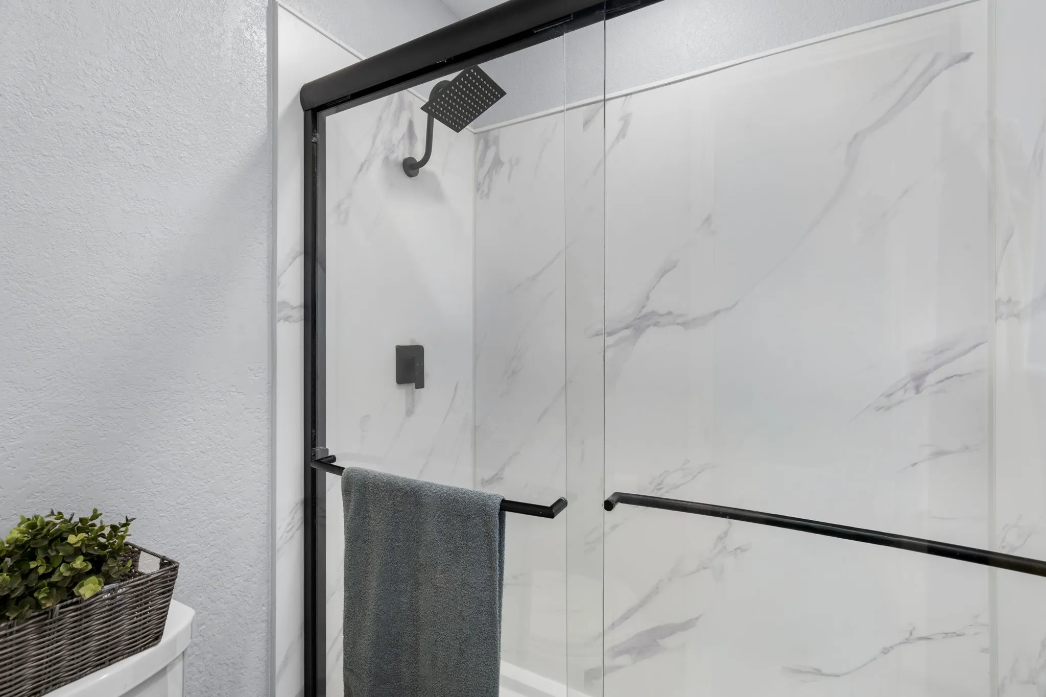 Shower enclosure with clear glass panels, matte black framing, and a matte black rainfall showerhead