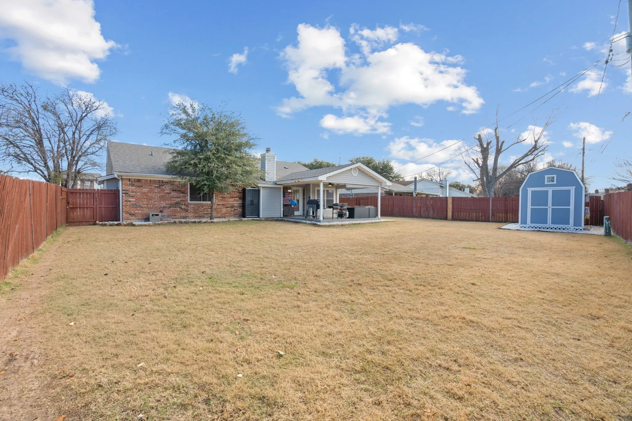 Expansive backyard featuring a large lawn, wood privacy fencing, a covered patio area, and a standalone storage shed