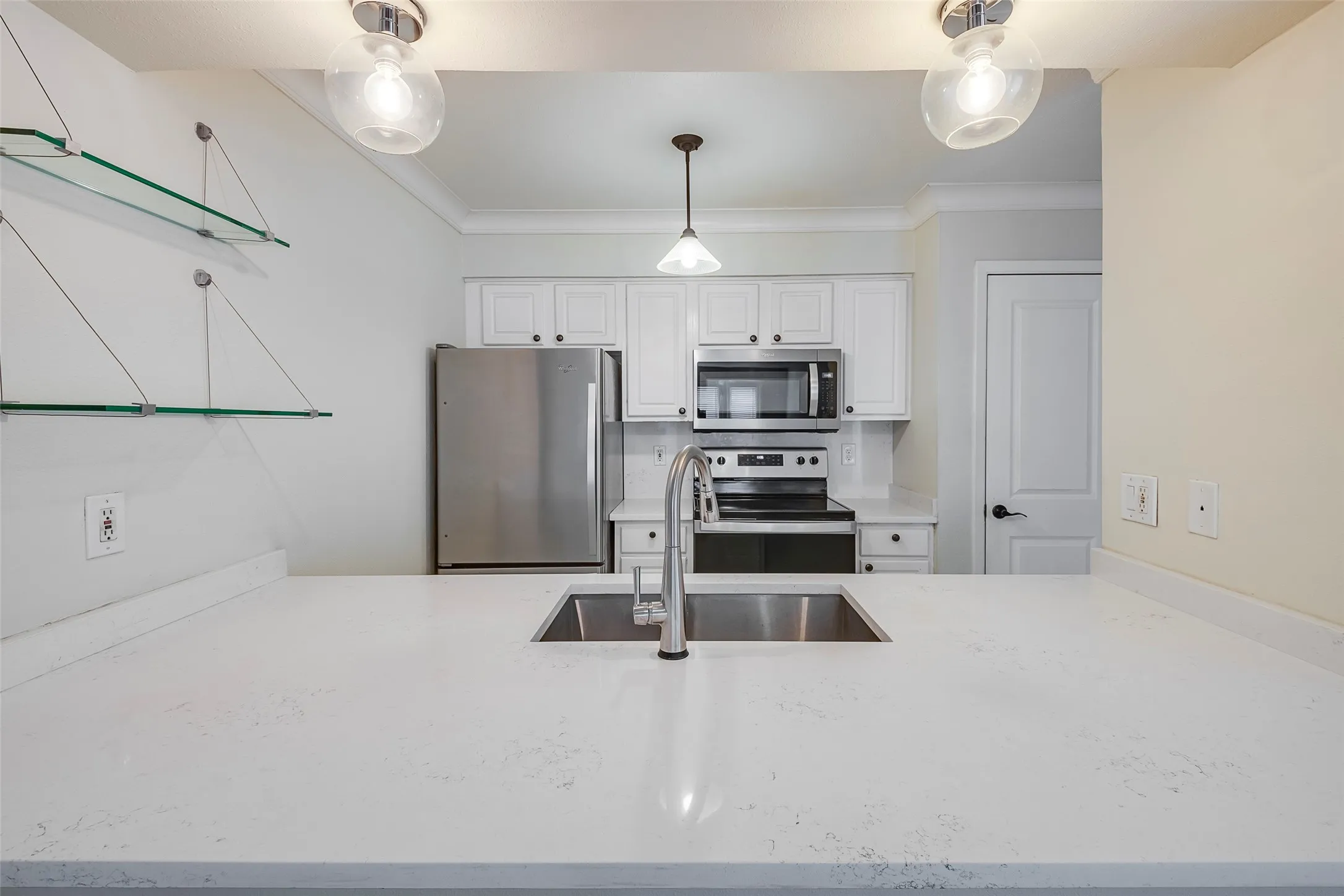 Kitchen with white cabinets, hanging light fixtures, sink, crown molding, and appliances with stainless steel finishes