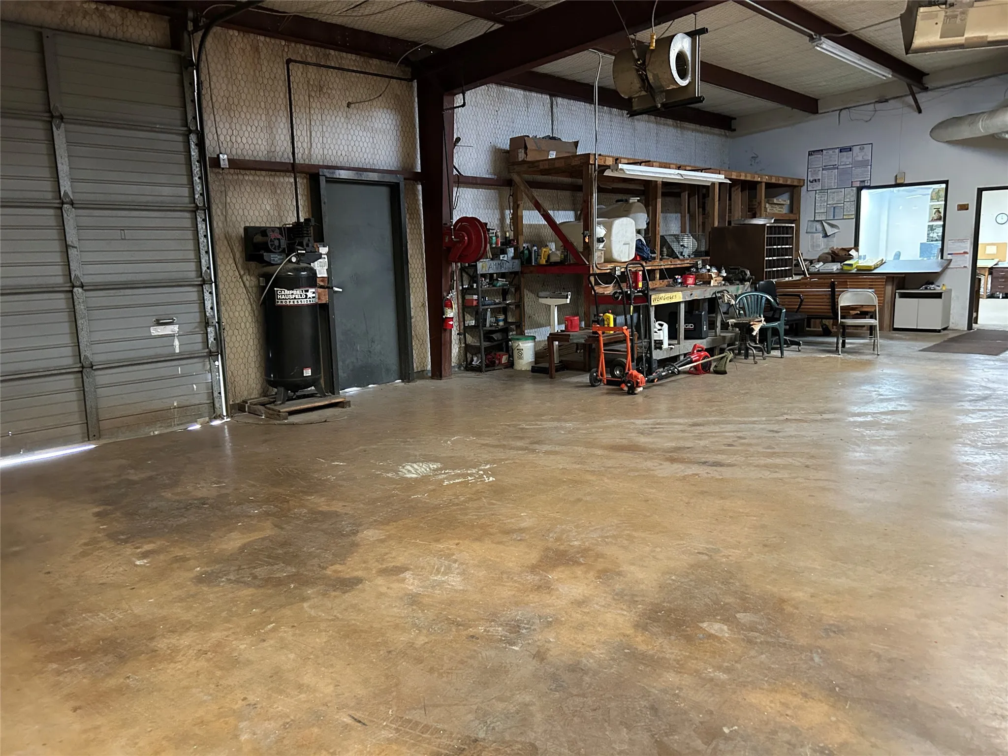Spacious industrial-style interior featuring a large roll-up door, concrete flooring, exposed metal framing, and fluorescent lighting