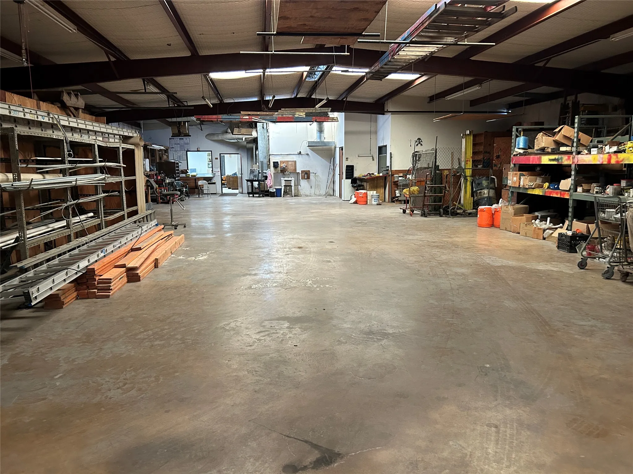 Spacious warehouse interior featuring a concrete floor, high ceilings with exposed structural beams, and fluorescent lighting