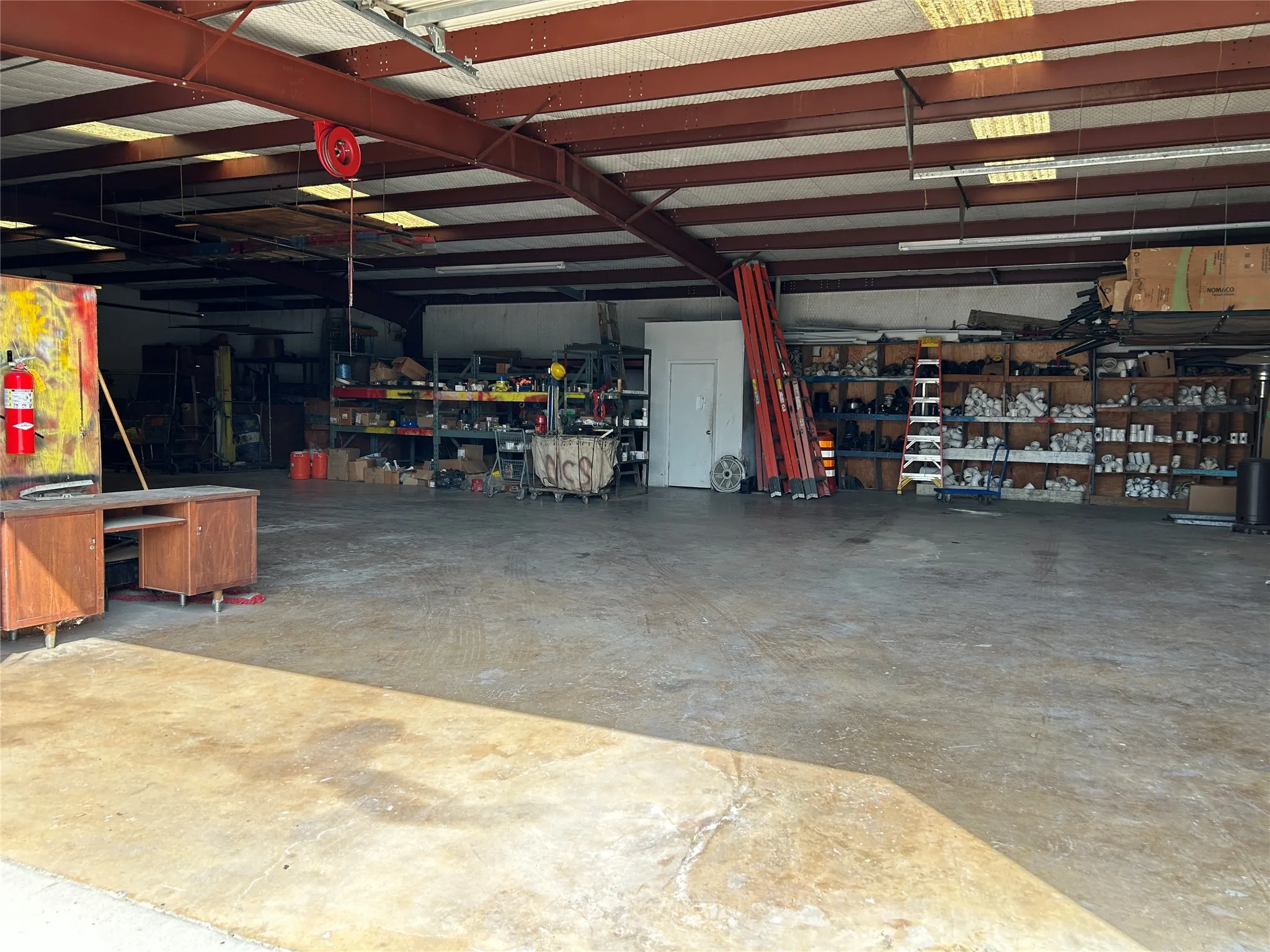 Spacious industrial interior featuring an open layout, concrete flooring, exposed metal ceiling beams, and integrated overhead lighting