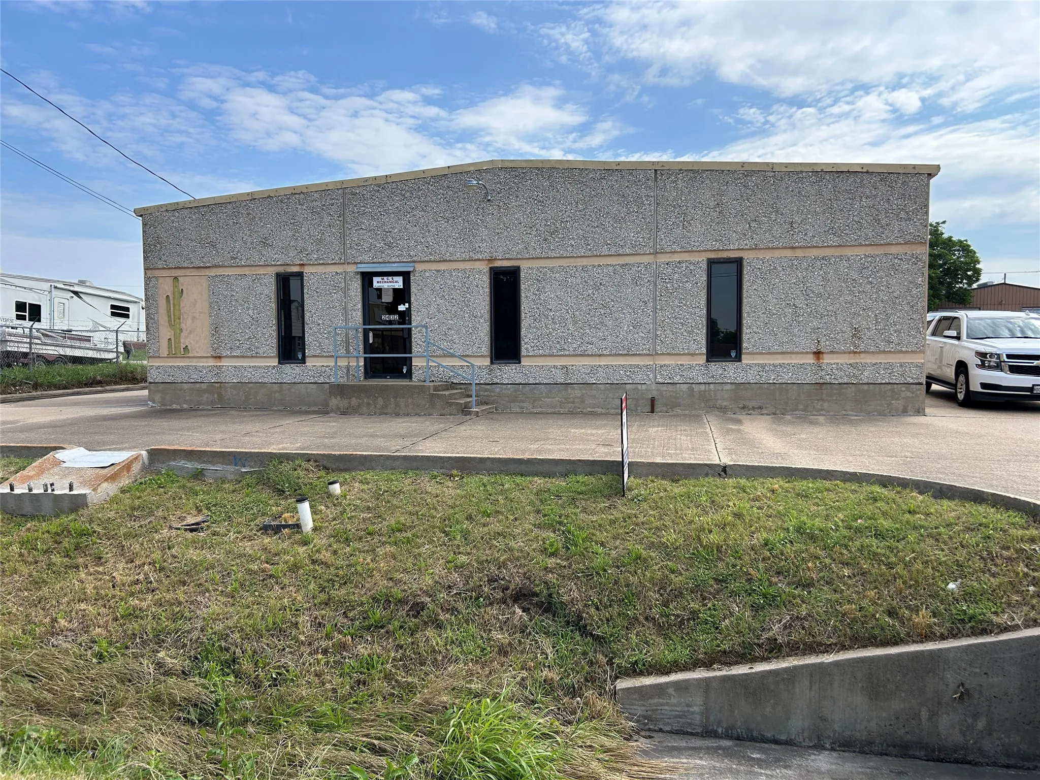 Commercial building featuring a textured facade, multiple windows, front entrance with handrails, and a concrete perimeter