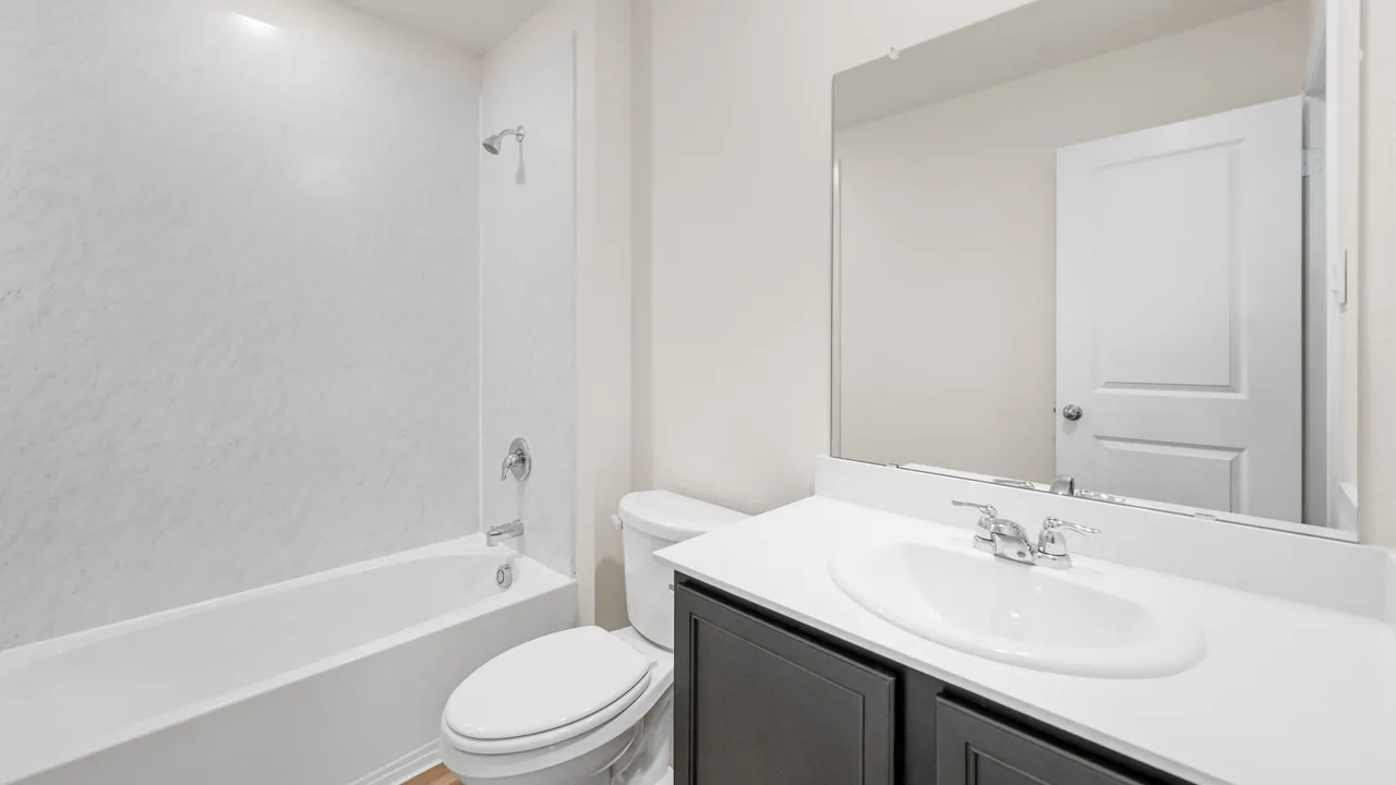 Contemporary bathroom featuring a white tub with shower, white toilet, and a vanity with dark cabinetry, white countertop, and an integrated sink