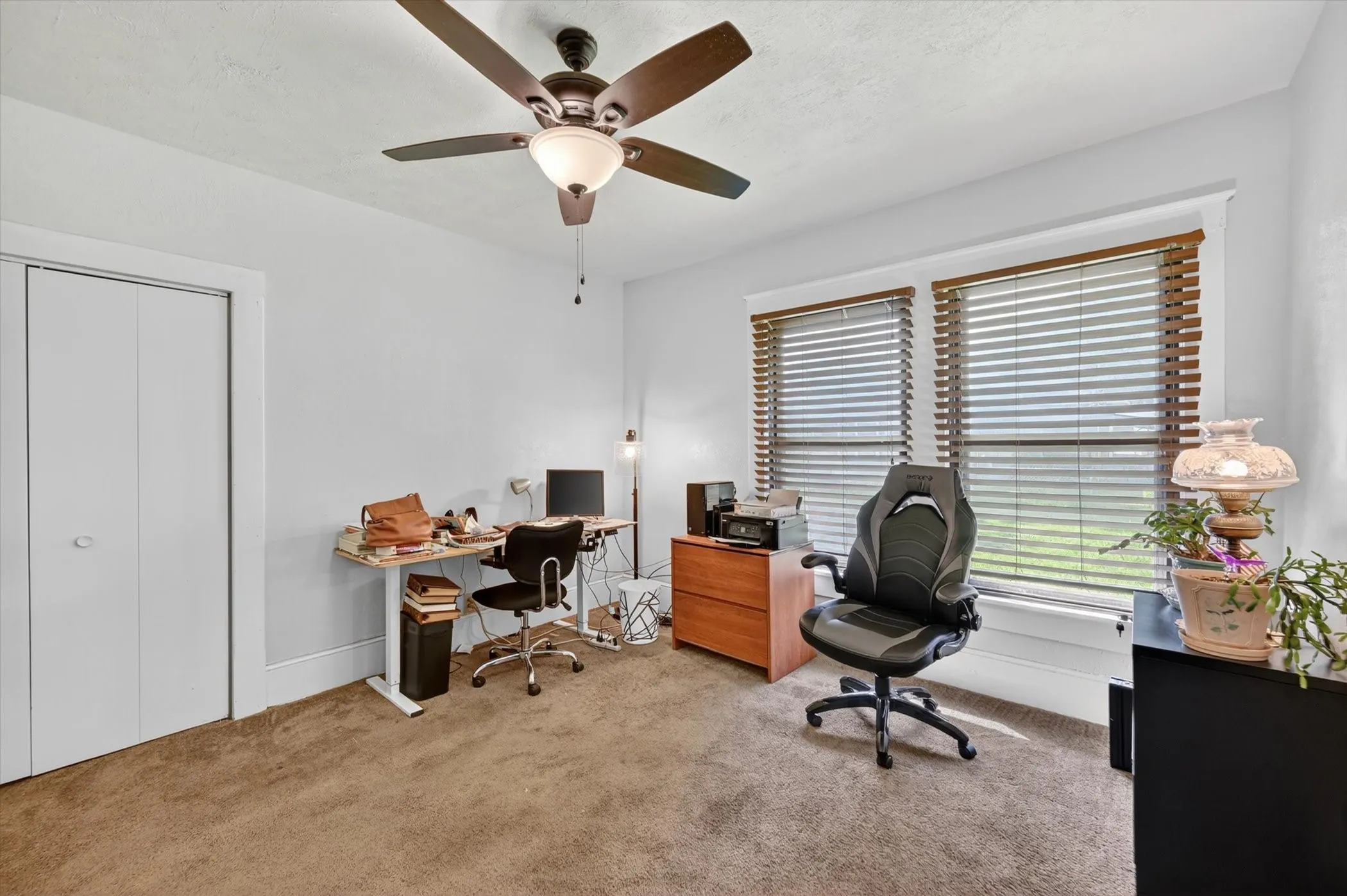 Carpeted room featuring a ceiling fan with integrated lighting, two windows with wood-tone blinds, white trim, and bi-fold closet doors