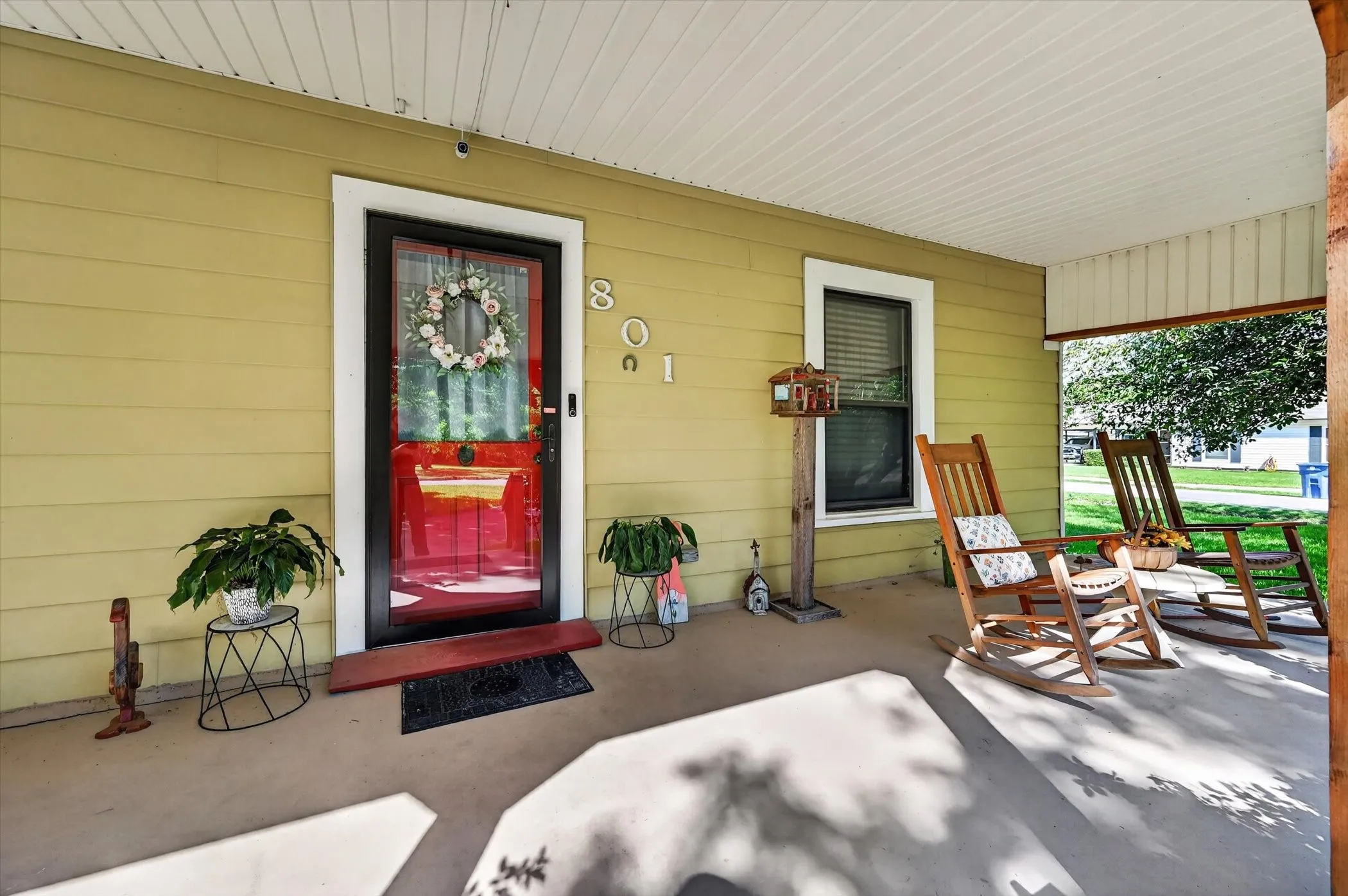 Covered porch with a vibrant red front door, light-colored siding, and a white soffit ceiling