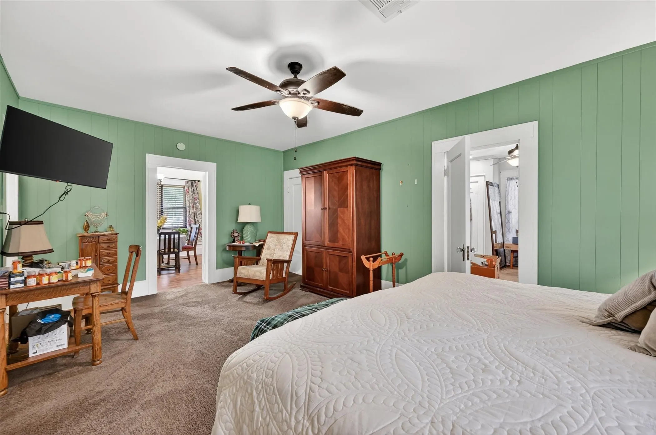 Spacious room featuring textured green paneling, neutral carpet, and a ceiling fan with integrated lighting