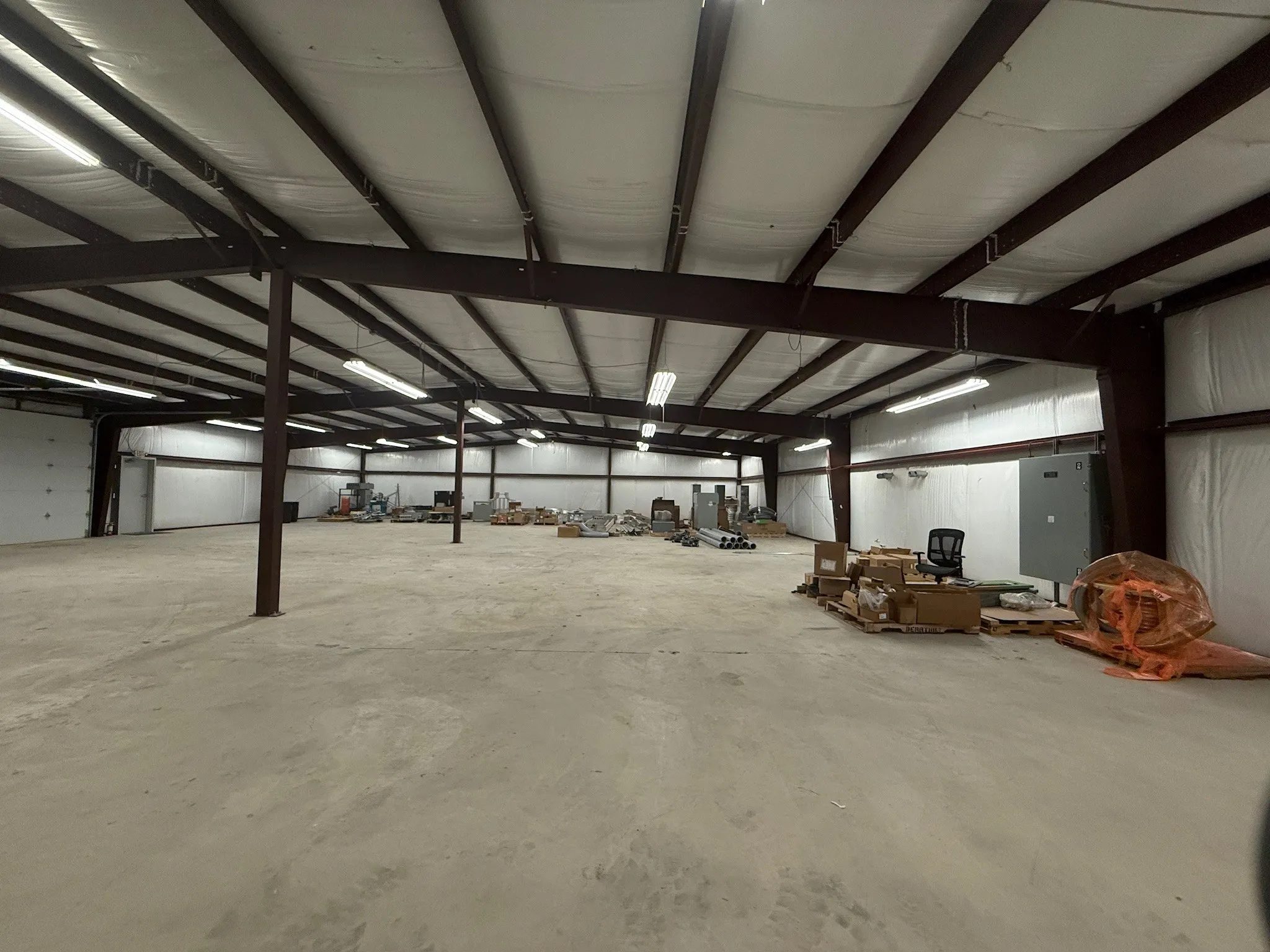 Expansive open warehouse space featuring concrete flooring and a high ceiling with exposed structural beams