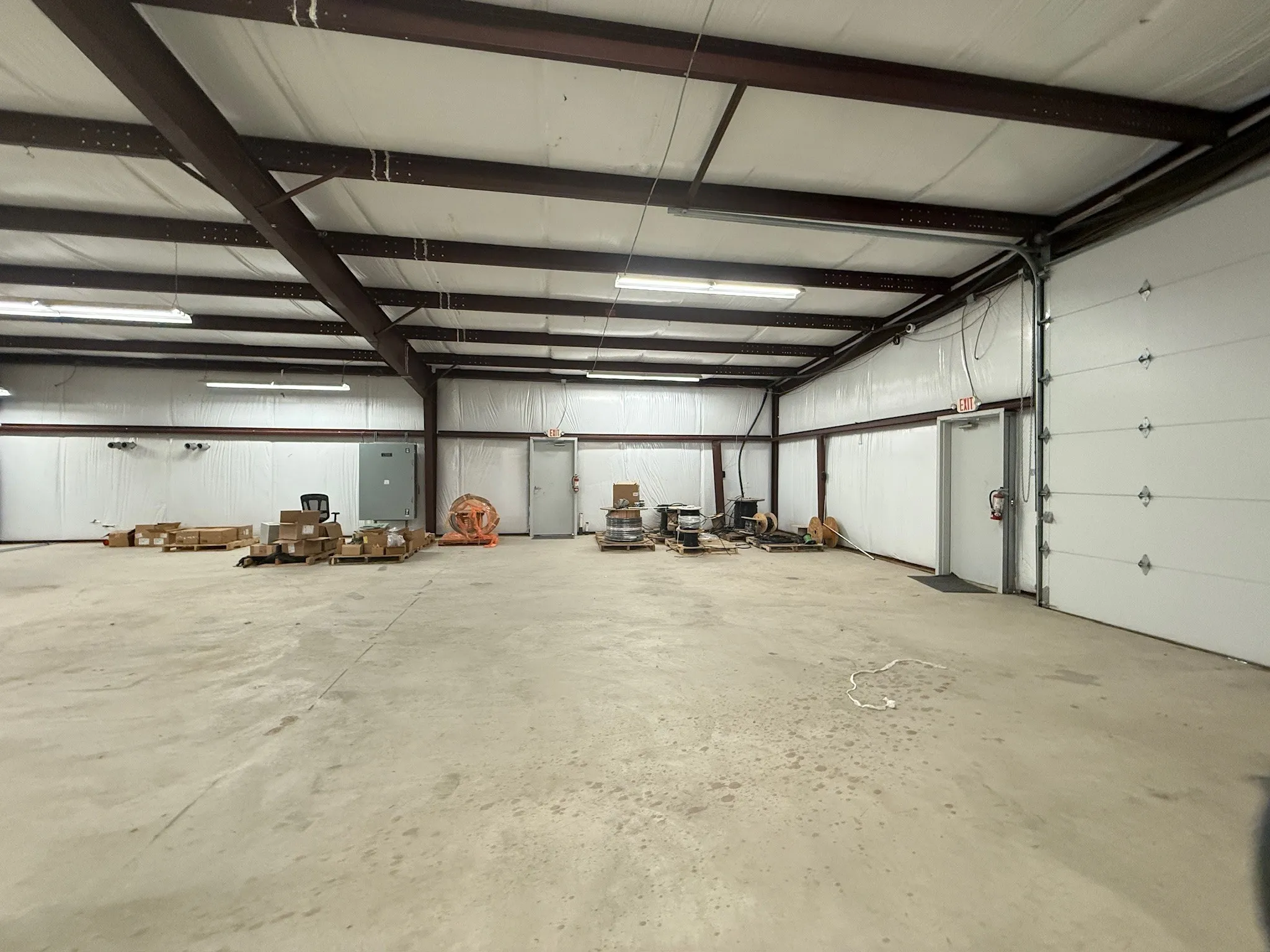 Spacious commercial interior featuring a concrete floor, exposed metal beam ceiling, and fluorescent lighting