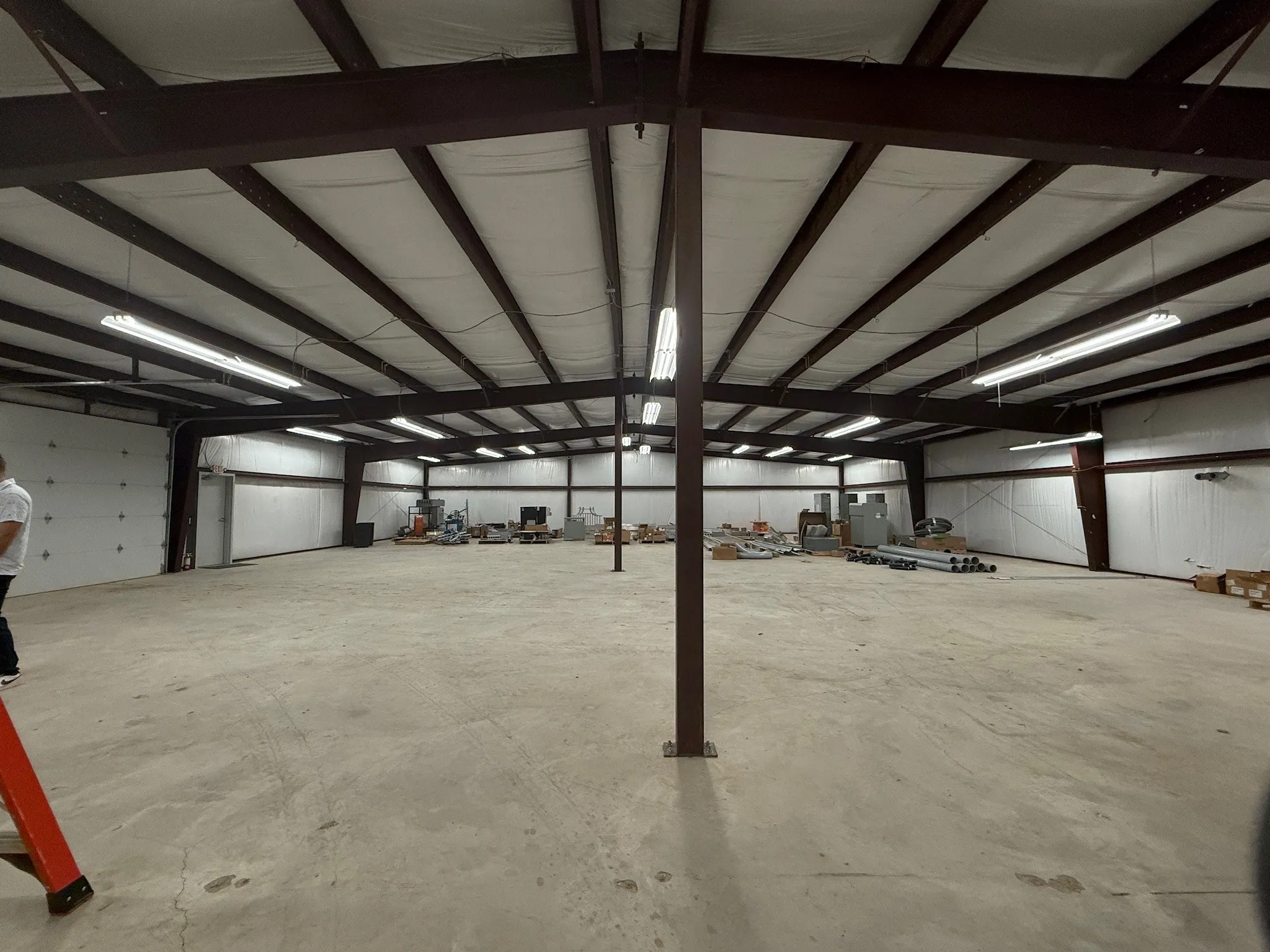 Spacious commercial warehouse featuring a high ceiling with exposed steel beams and ample fluorescent lighting