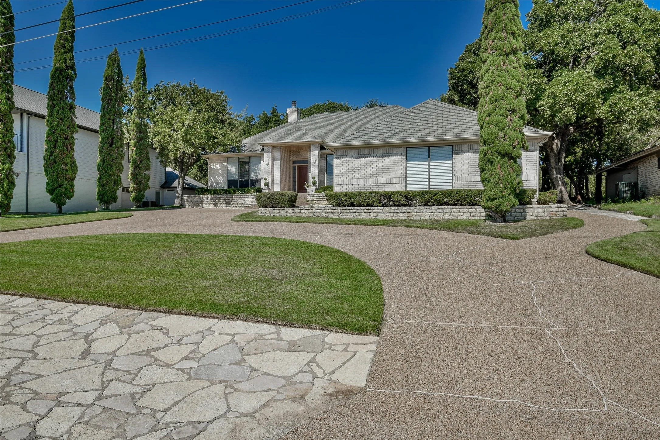 View of front of home with a front yard, a chimney, curved driveway, and brick siding