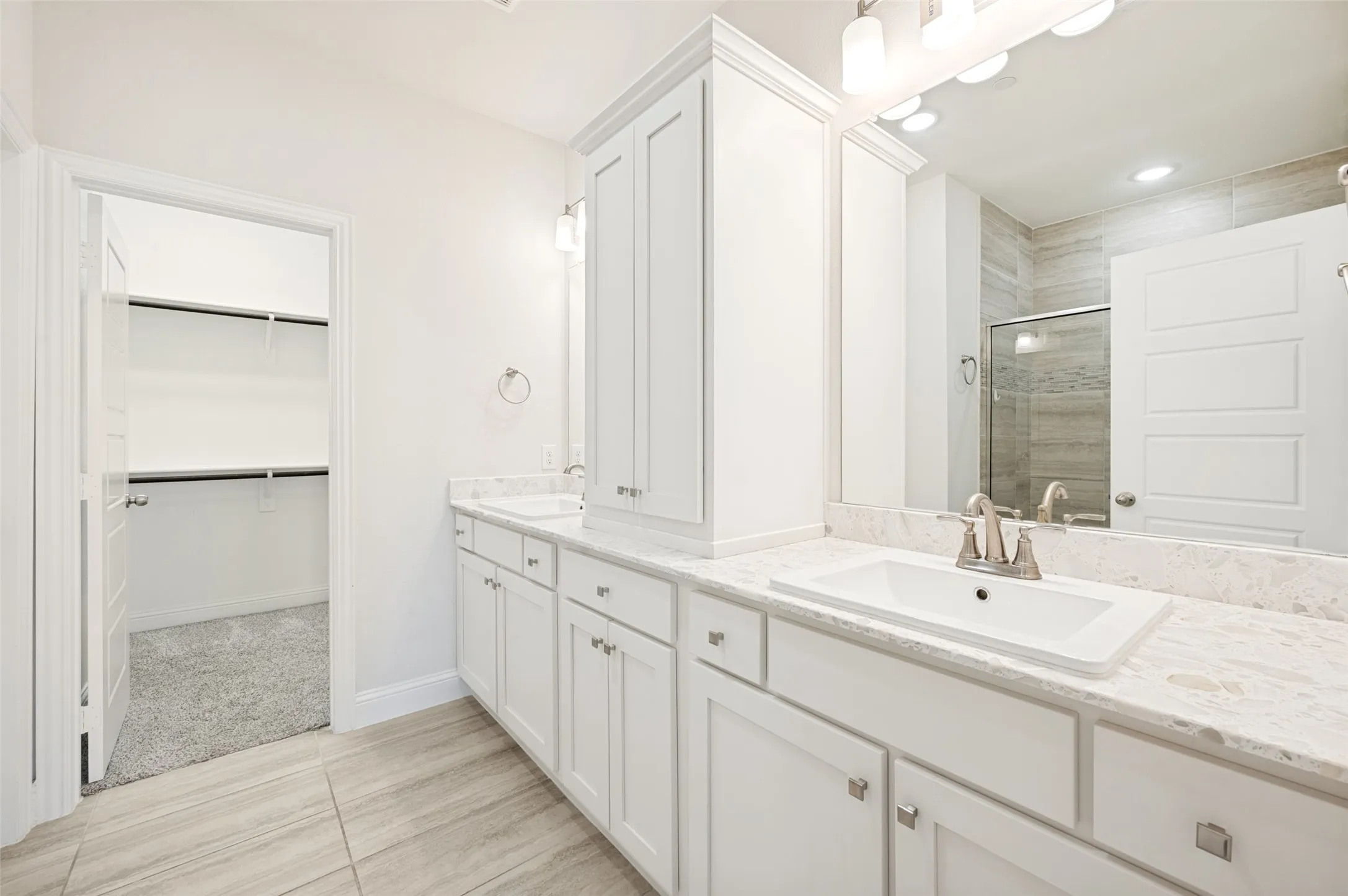 Bathroom featuring dual rectangular sinks set into stone-finish countertops, extensive white cabinetry, a large vanity mirror, and tile flooring