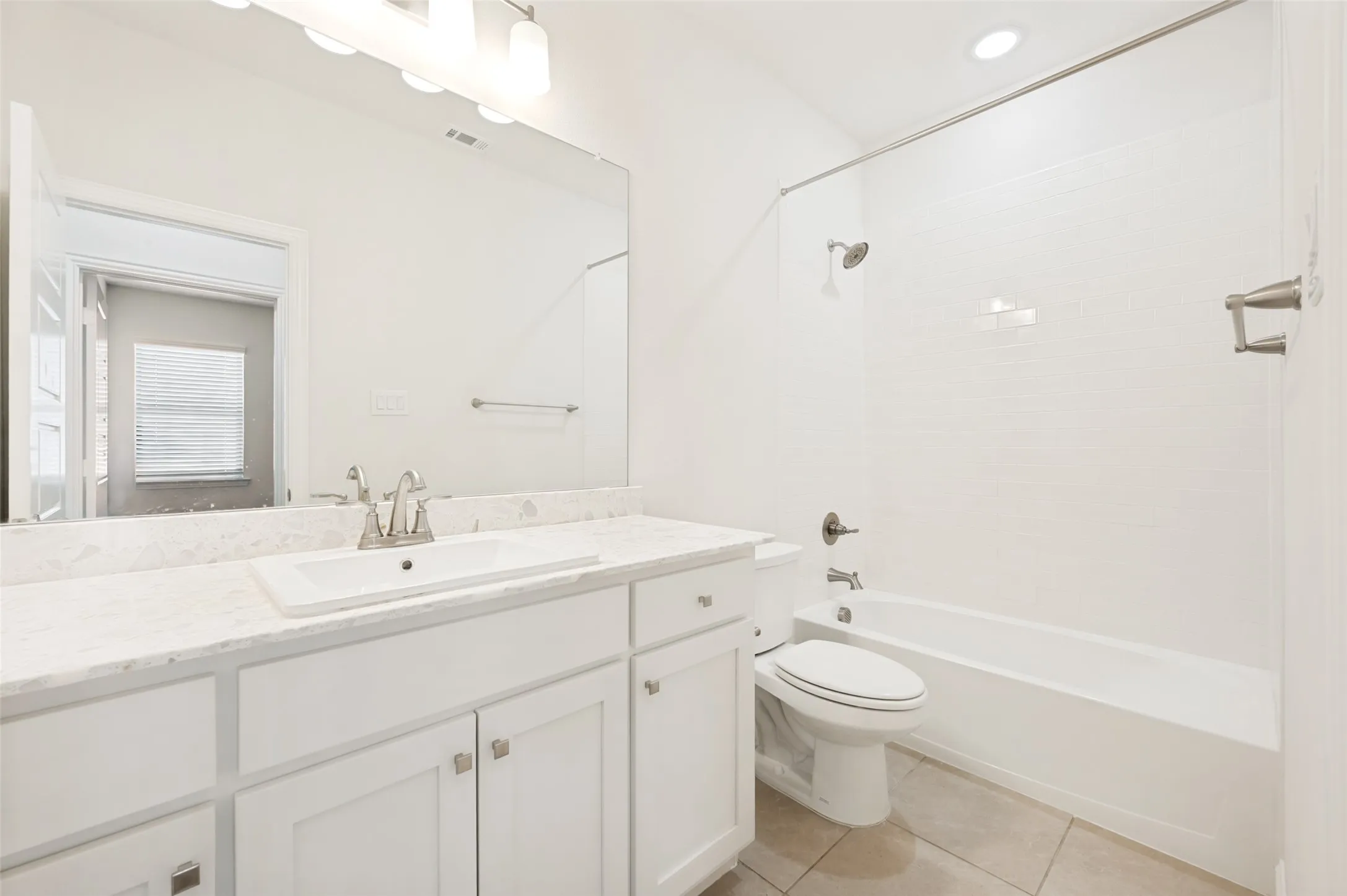 Bathroom featuring a white vanity with an undermount sink, a light-toned countertop, a large wall-mounted mirror, and a shower-over-tub combination with subway tile surround