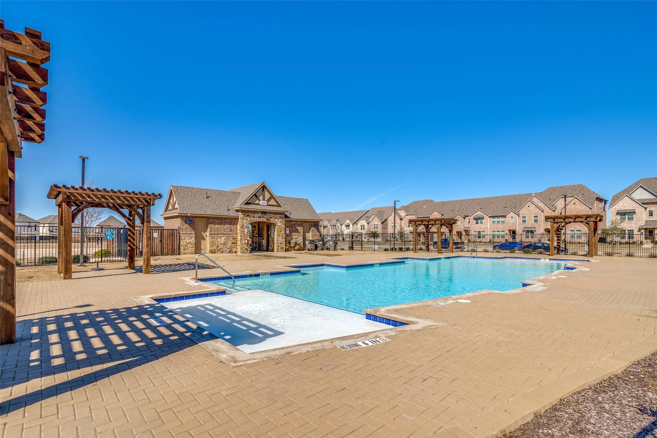 Community pool featuring a stone and brick clubhouse building, multiple pergola structures, and a surrounding paved deck
